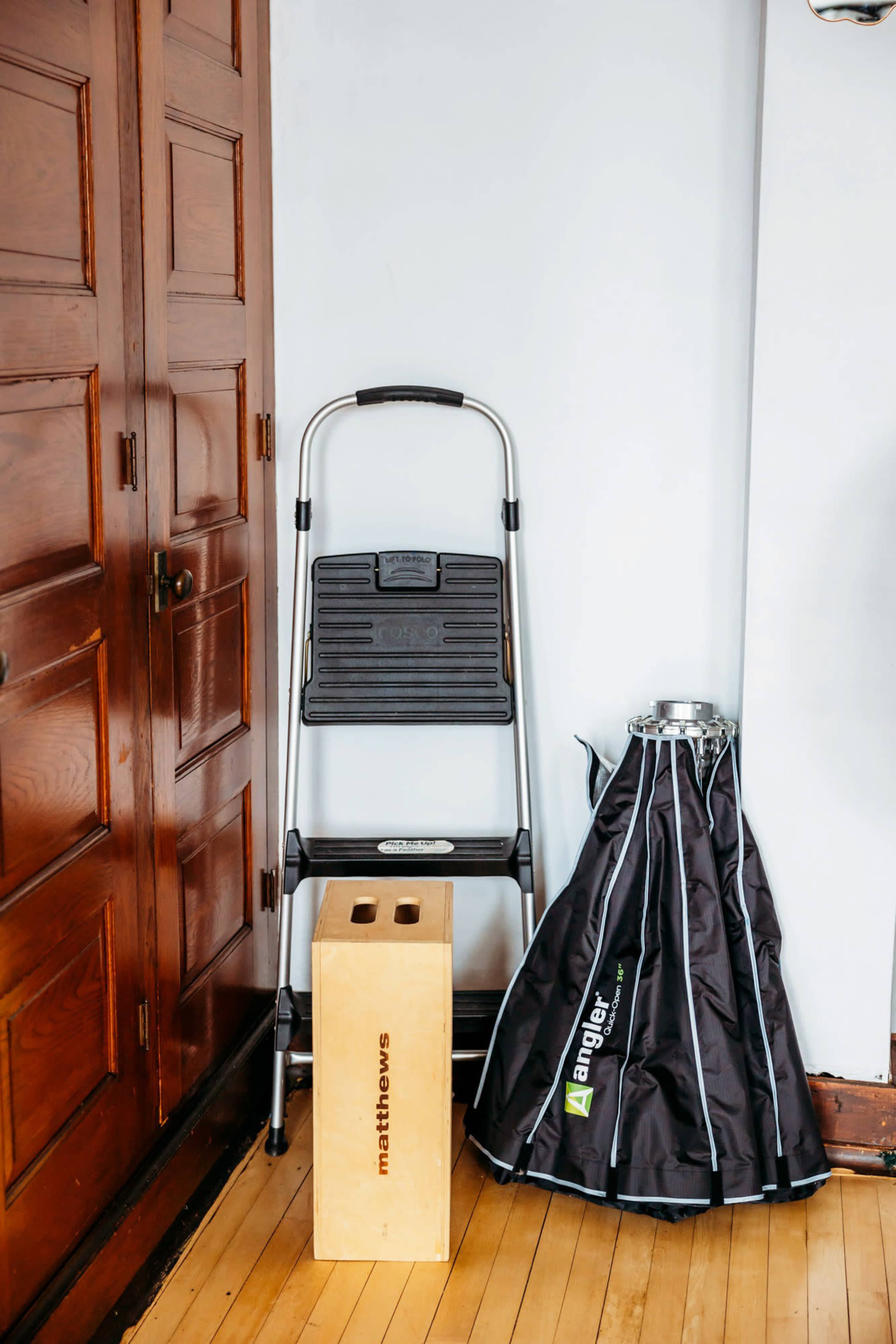 A metal step ladder is positioned next to a wooden stool and a folded umbrella in a room with wooden walls.