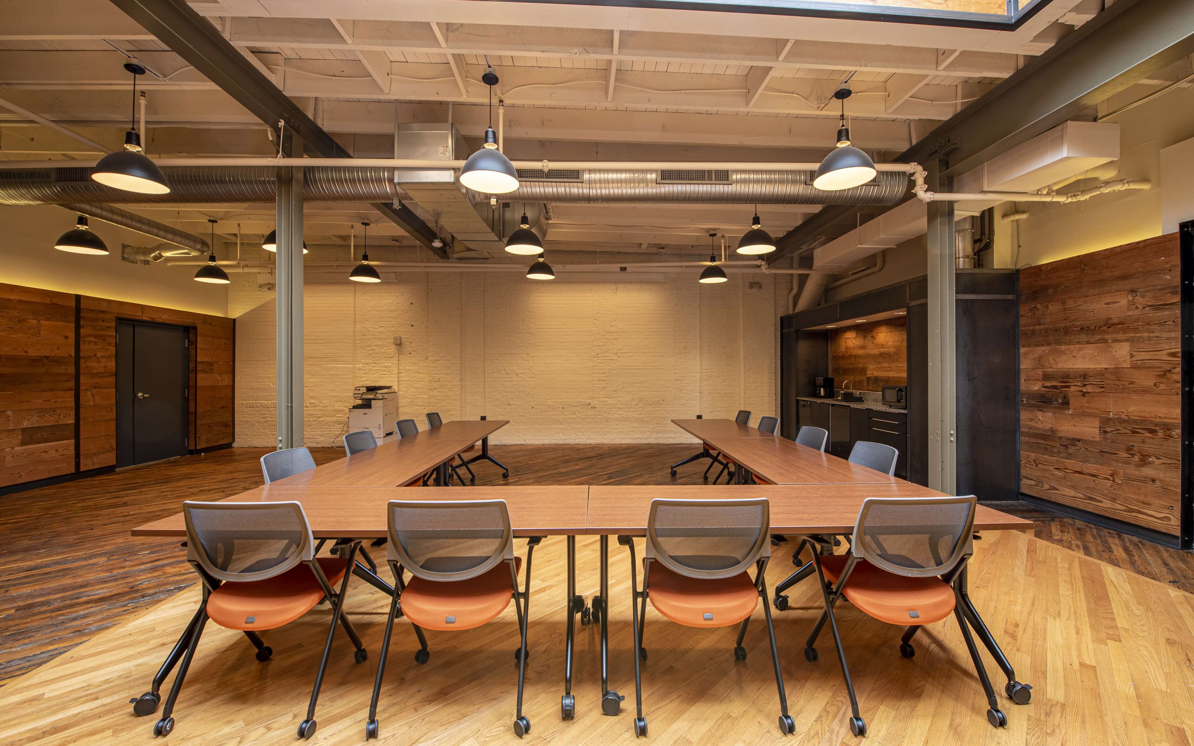 A modern conference room features a long rectangular table surrounded by chairs, with wooden walls and overhead lighting.