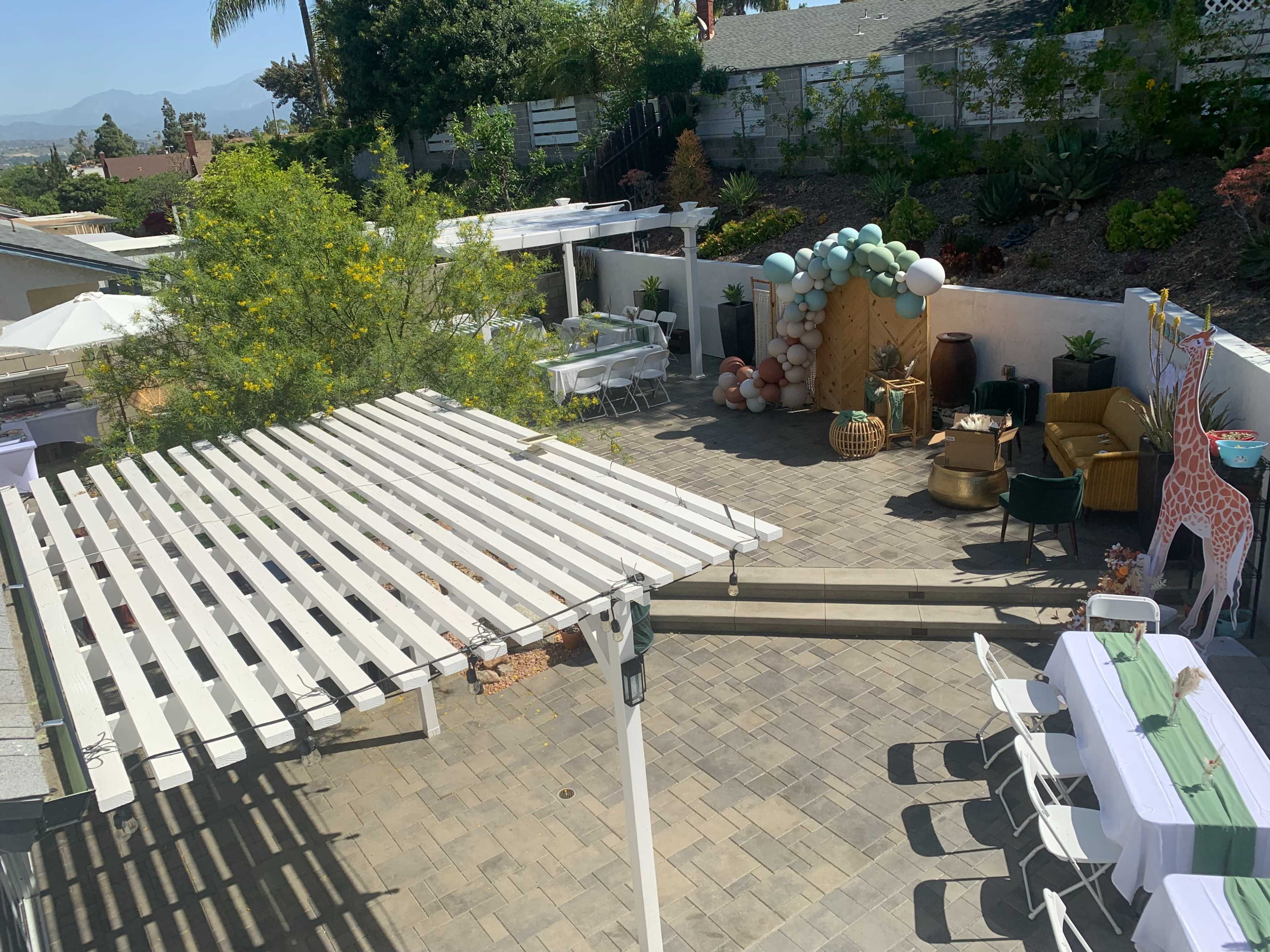 A backyard patio area featuring multiple seating arrangements, a decorative balloon display, and shaded pergolas.