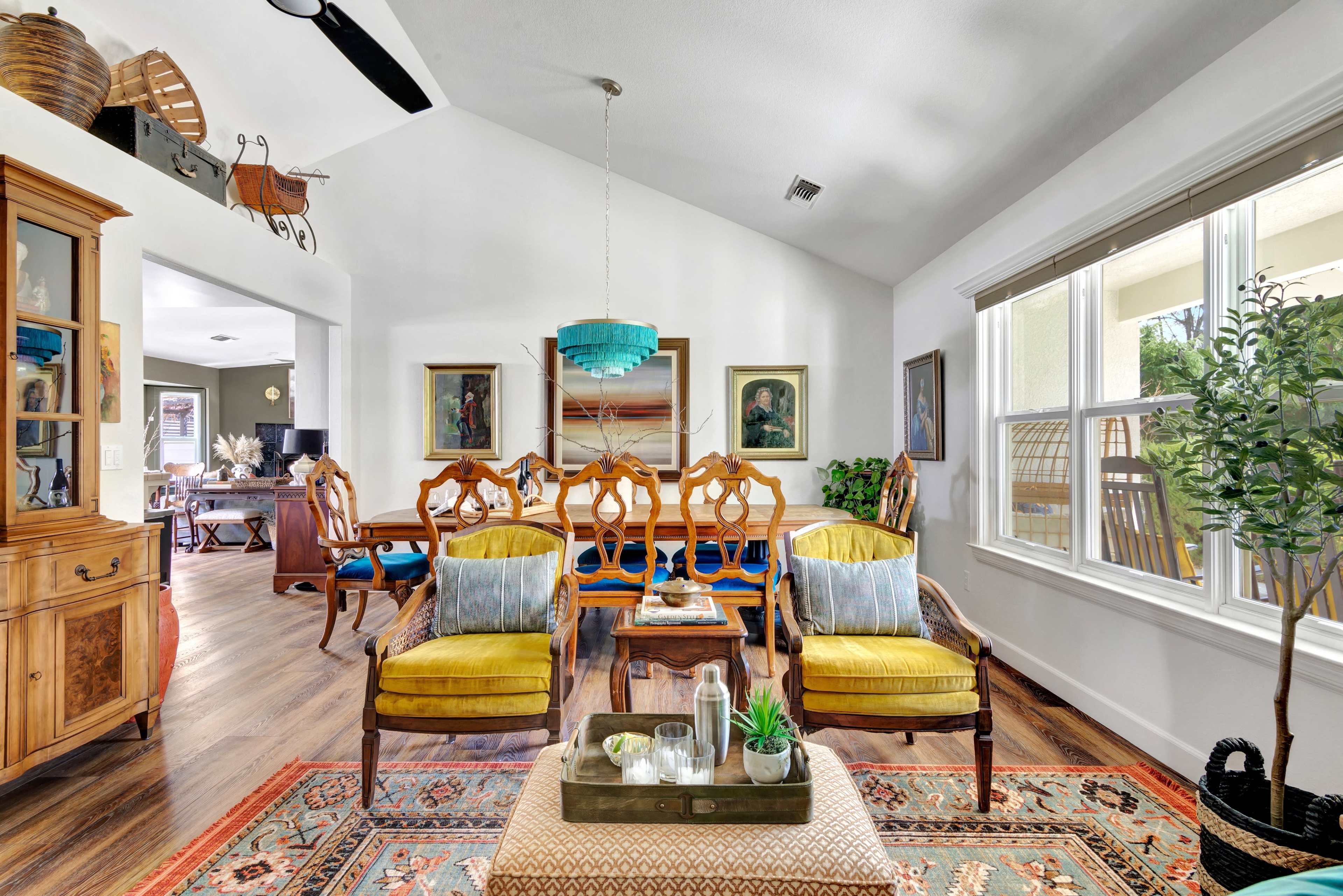 A bright living room features seating arrangements with yellow chairs, a wooden coffee table, and artwork on the walls, all beneath a high ceiling.