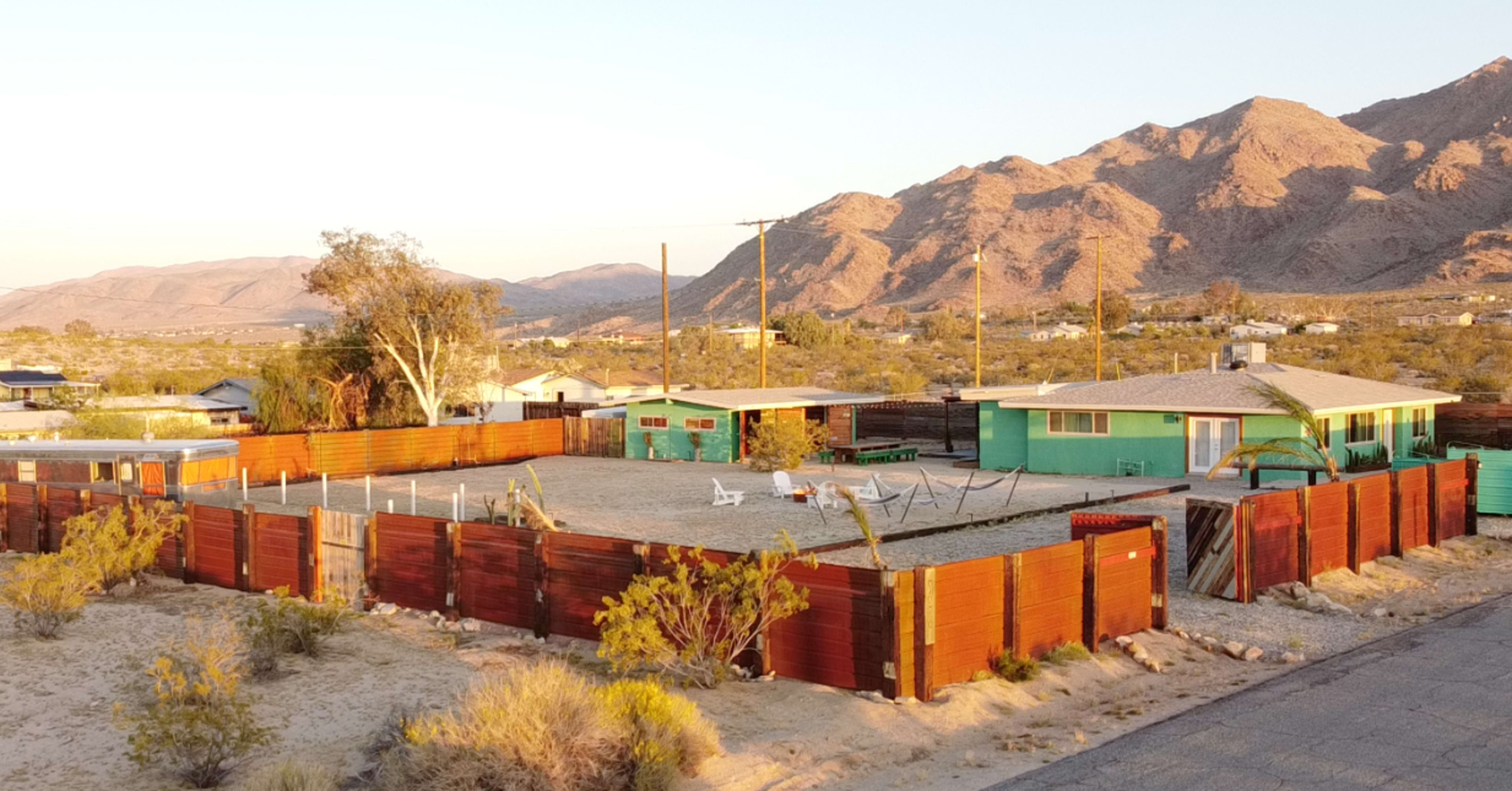 A fenced property with two buildings, a sandy area, and mountains in the background.