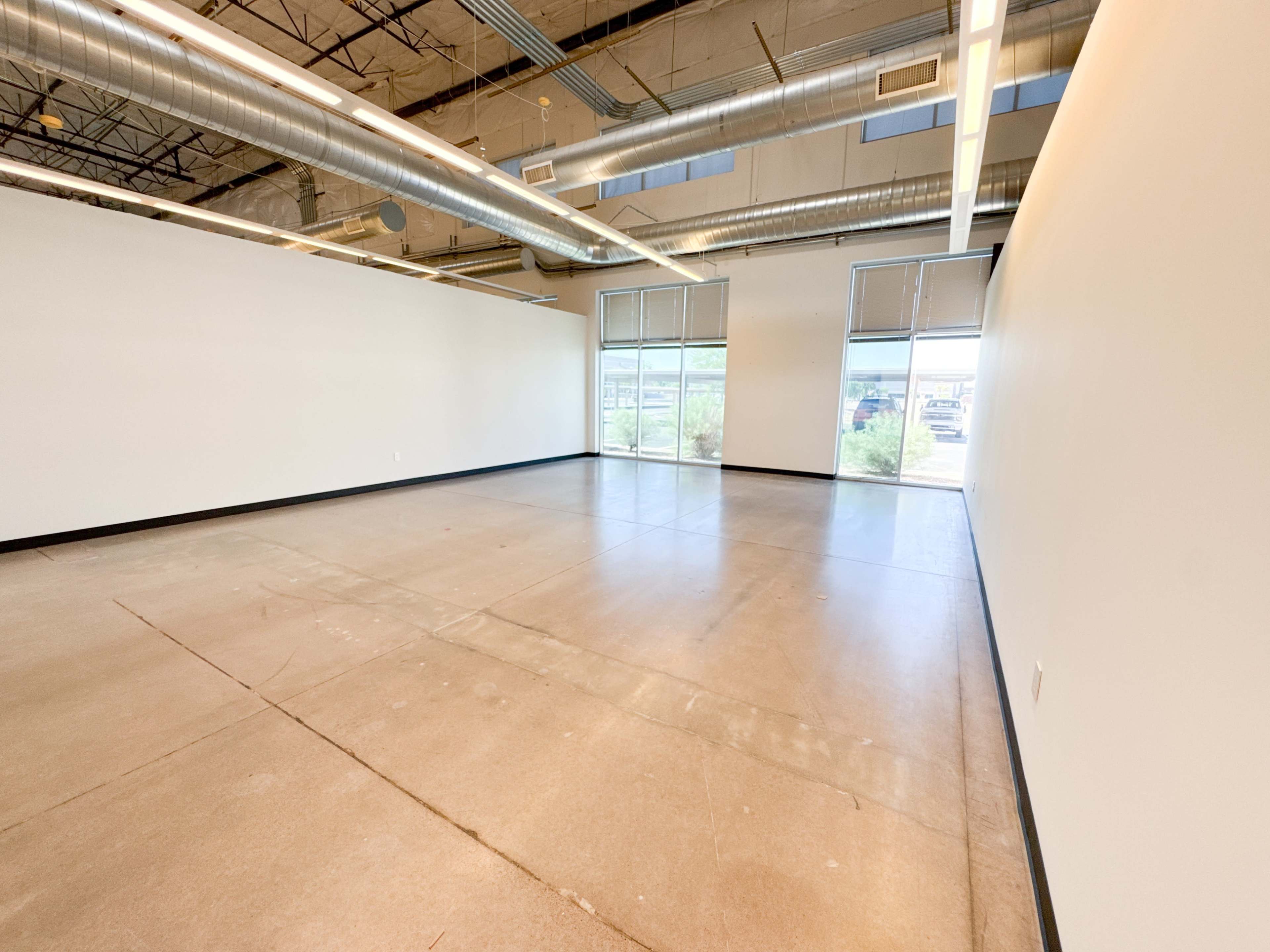 The image shows an empty room with concrete flooring and large windows on one side, illuminated by natural light.