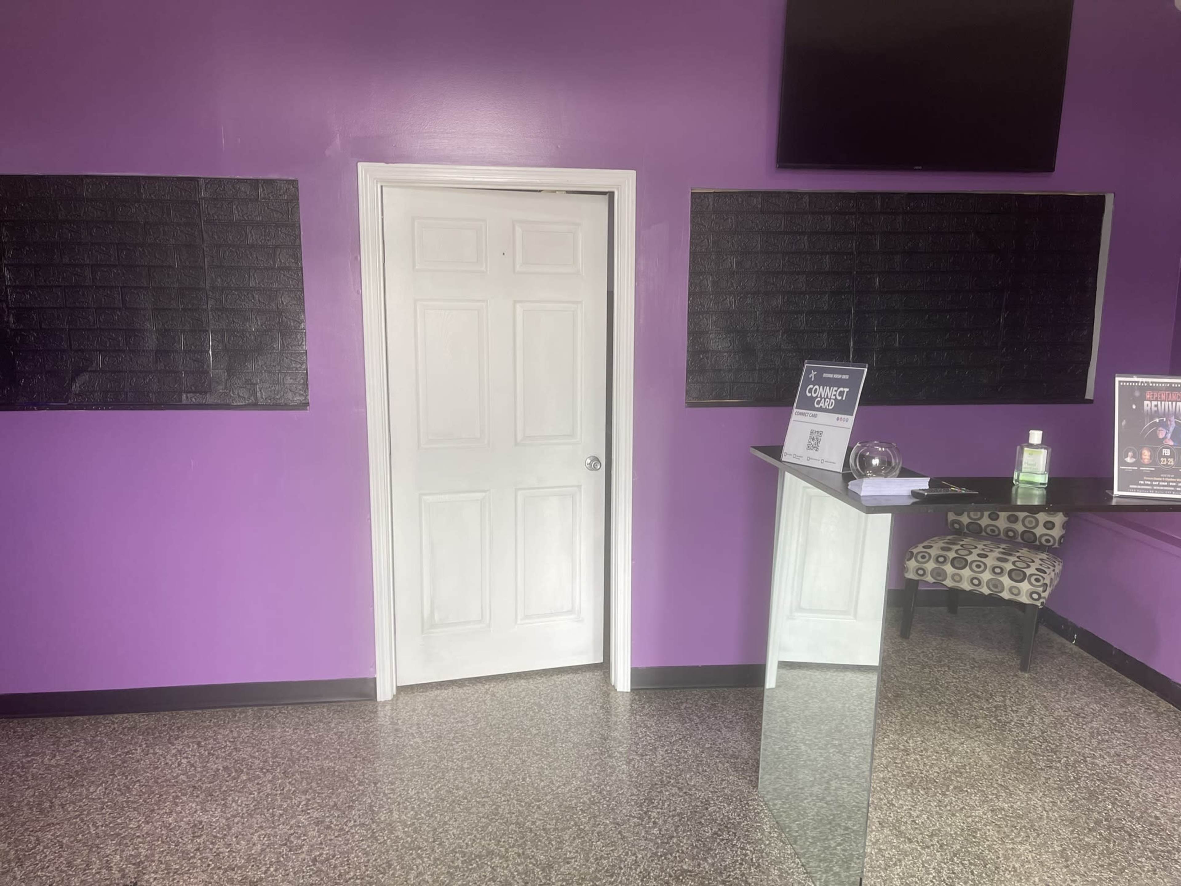 A room with purple walls, a white door, and a glass reception desk accompanied by a chair.