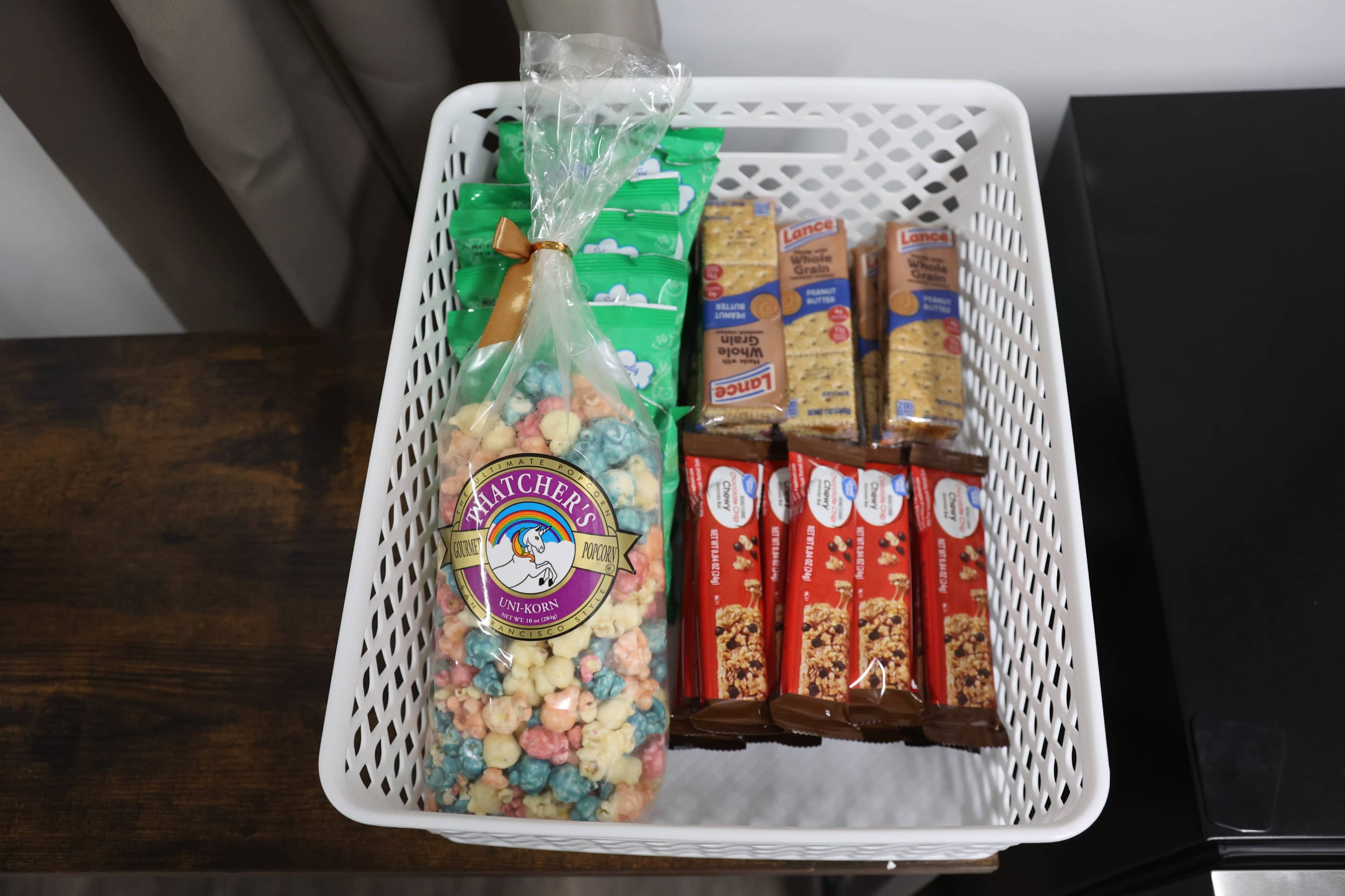 A white basket contains colorful popcorn, snack bars, and a few packets of food items.