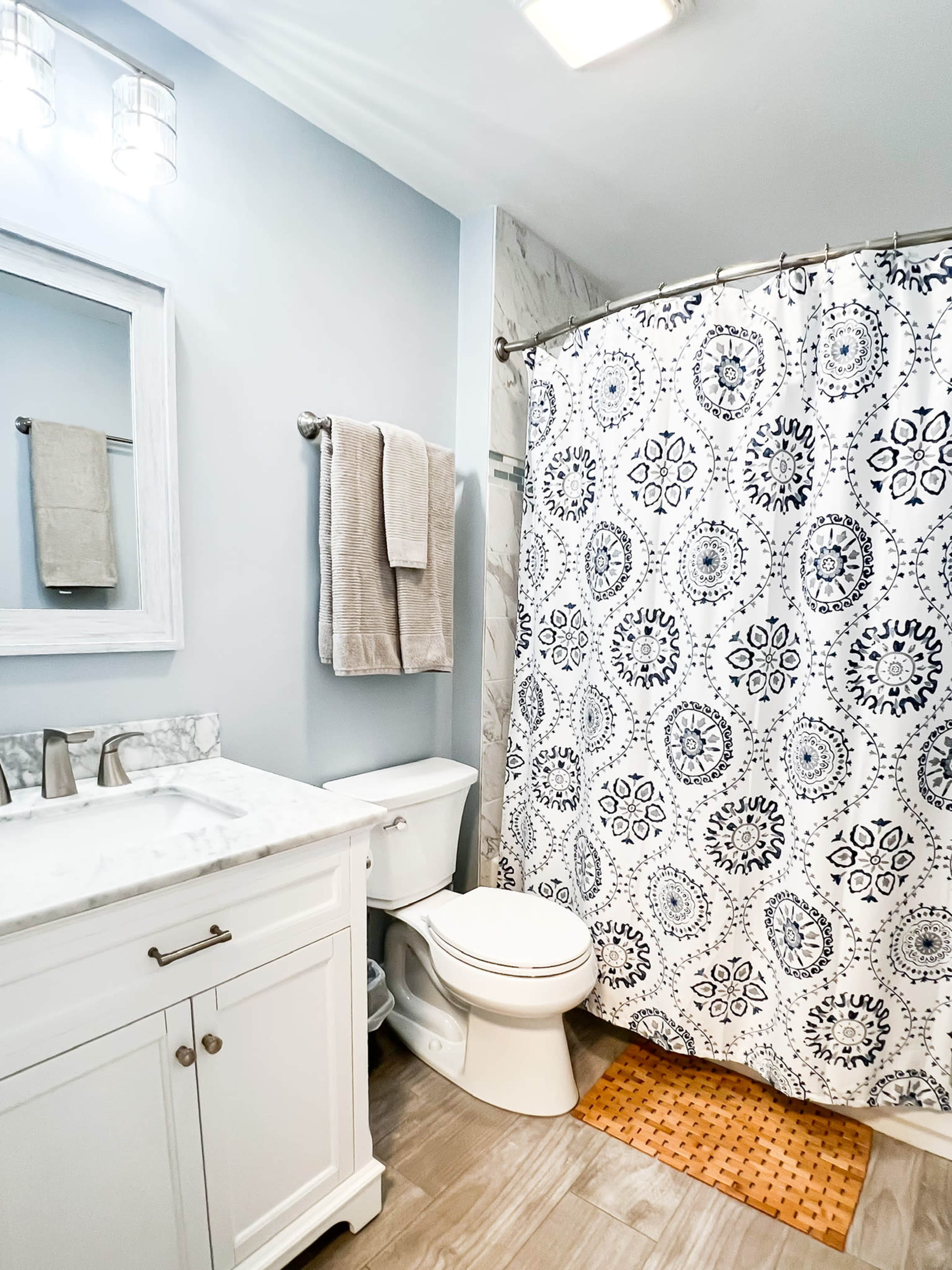 A modern bathroom with a white vanity, a floral shower curtain, a toilet, and light-colored walls.