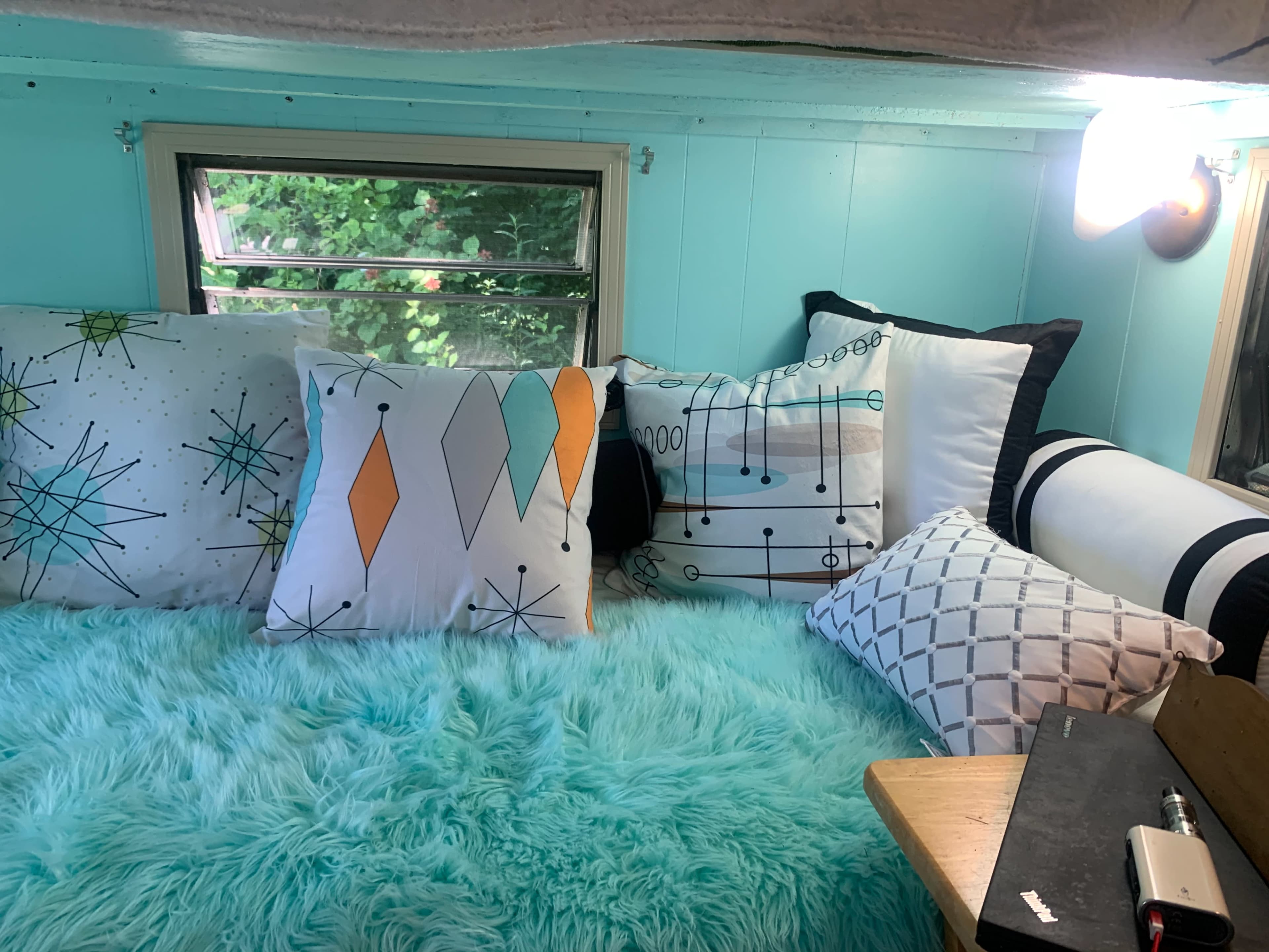 A cozy sleeping area features a collection of colorful pillows and a fluffy blue blanket beneath a window.