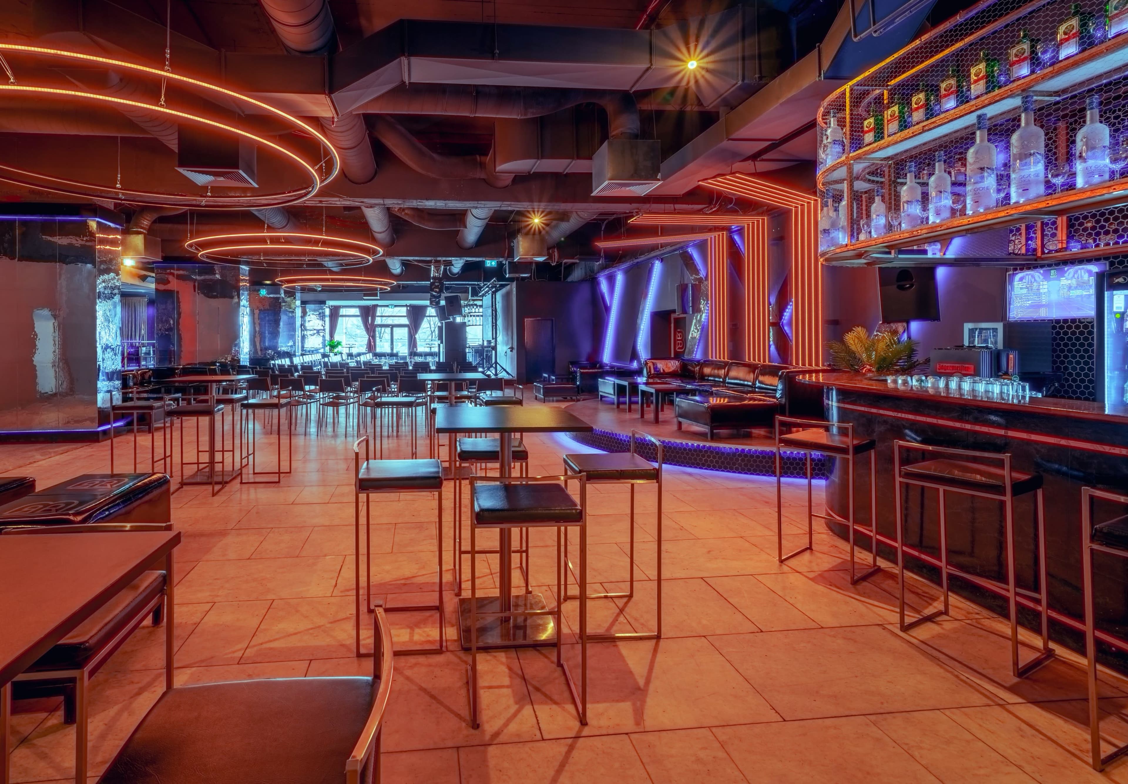 A modern bar interior with illuminated seating areas, a well-stocked bar, and geometric lighting designs.