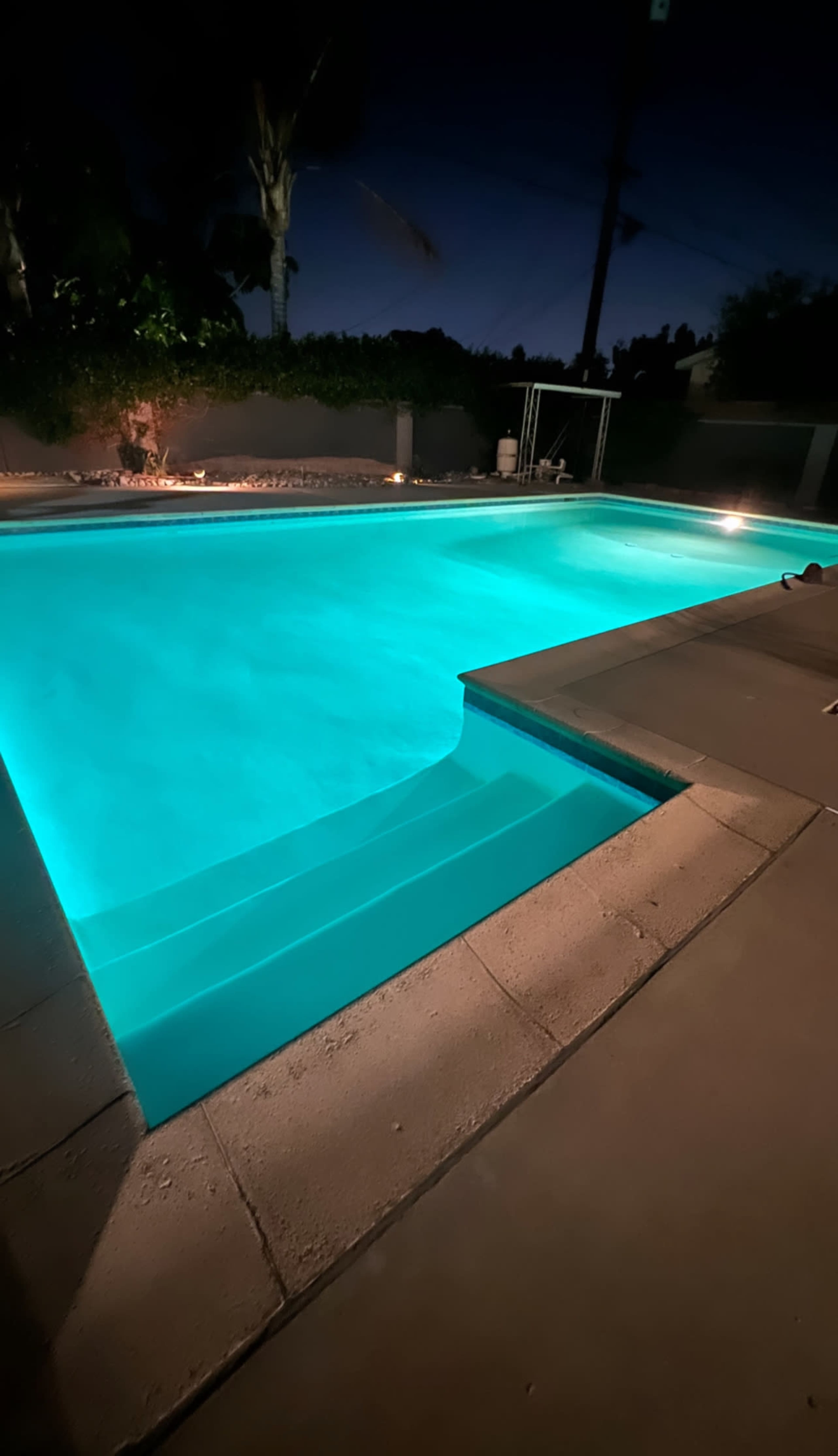 A well-lit swimming pool at night with a stepped entry and surrounding illuminated patio.