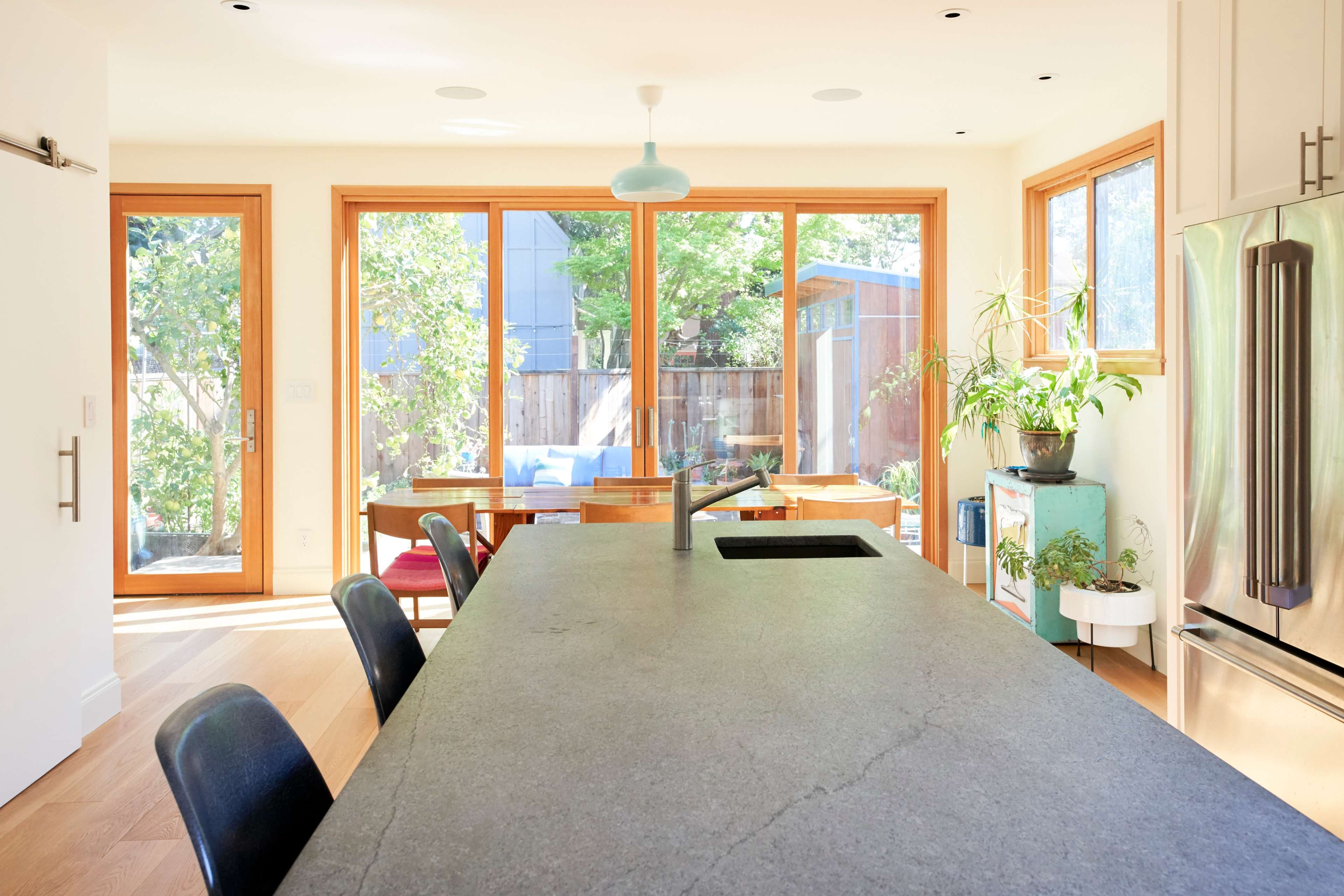 A modern kitchen with a large stone island, large windows overlooking a garden, and minimalist decor.