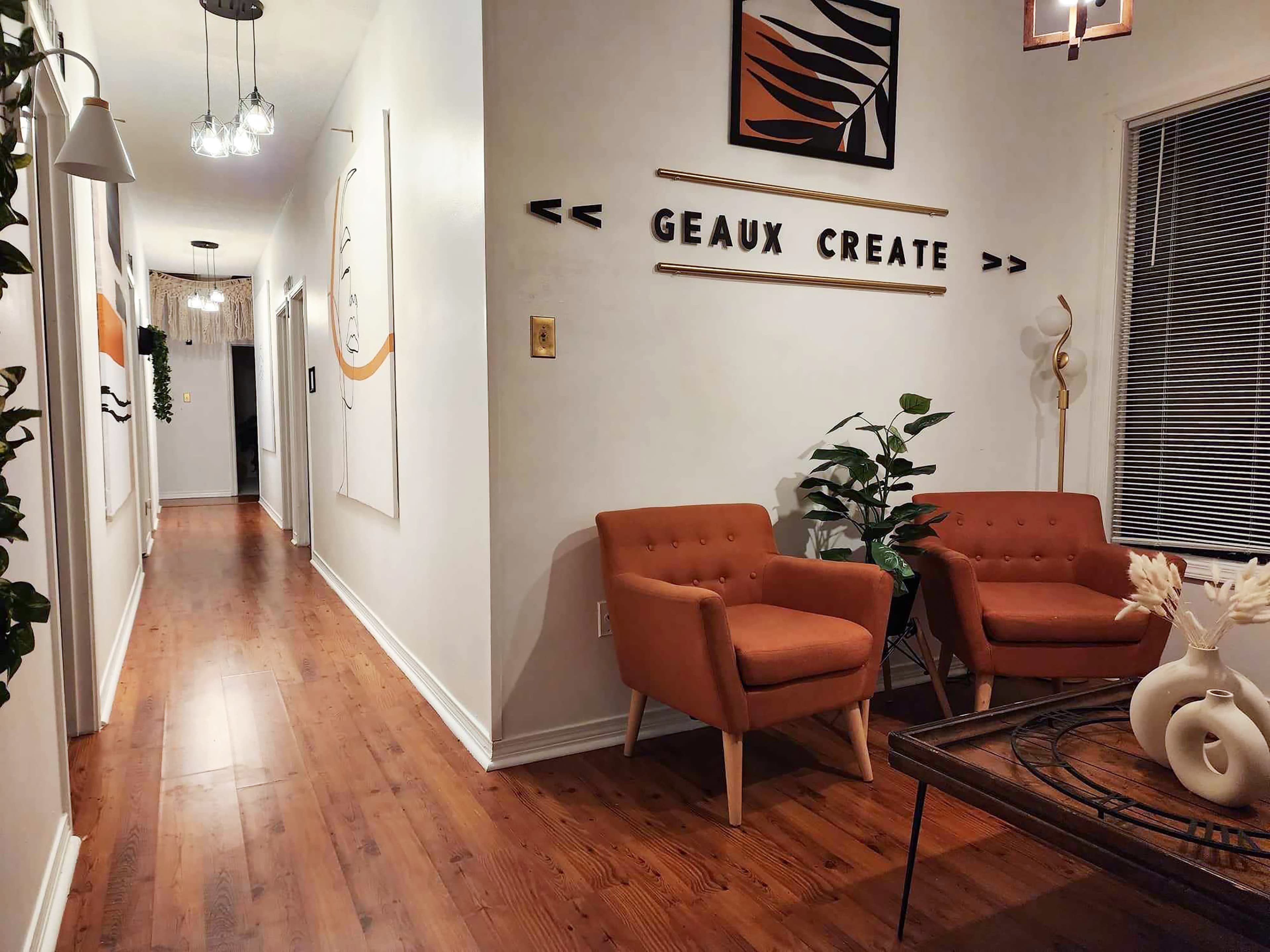 The image shows a well-lit hallway with a pair of orange armchairs and decorative wall art, leading to a distant door.
