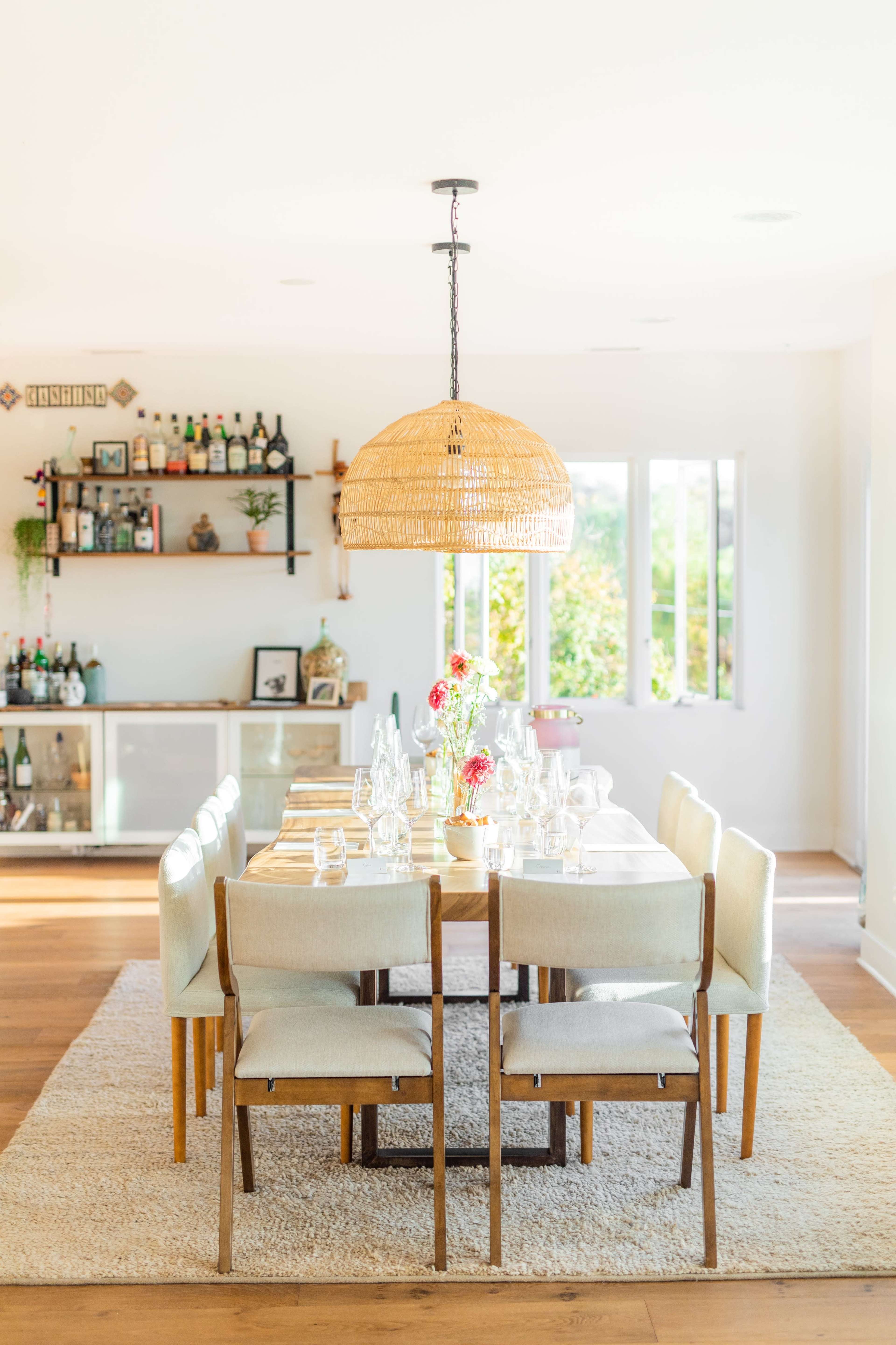 A spacious dining room features a long wooden table set with glassware and a large woven pendant light overhead.