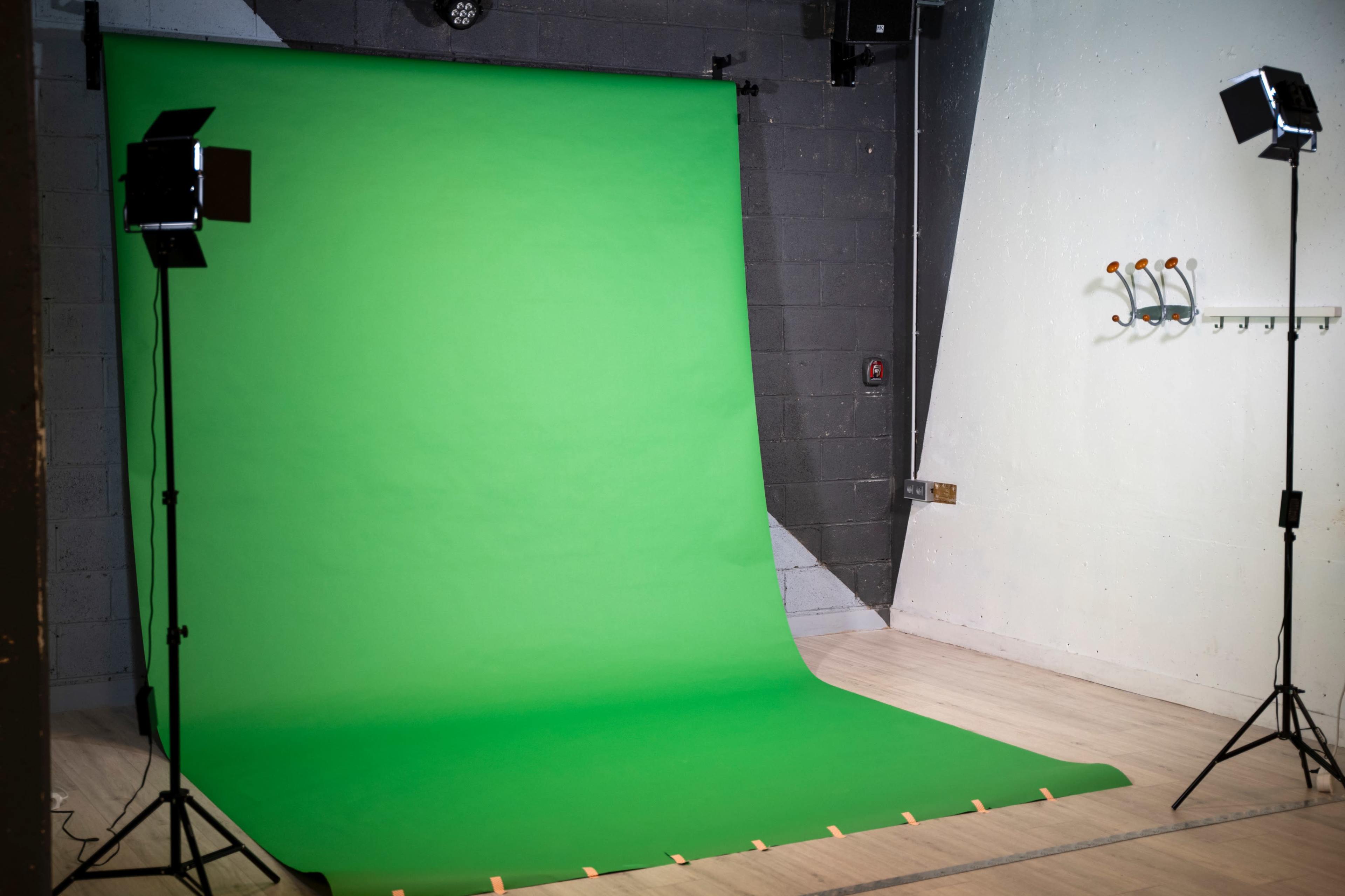 A studio setup featuring a large green backdrop, two lights on stands, and a wall with hooks.