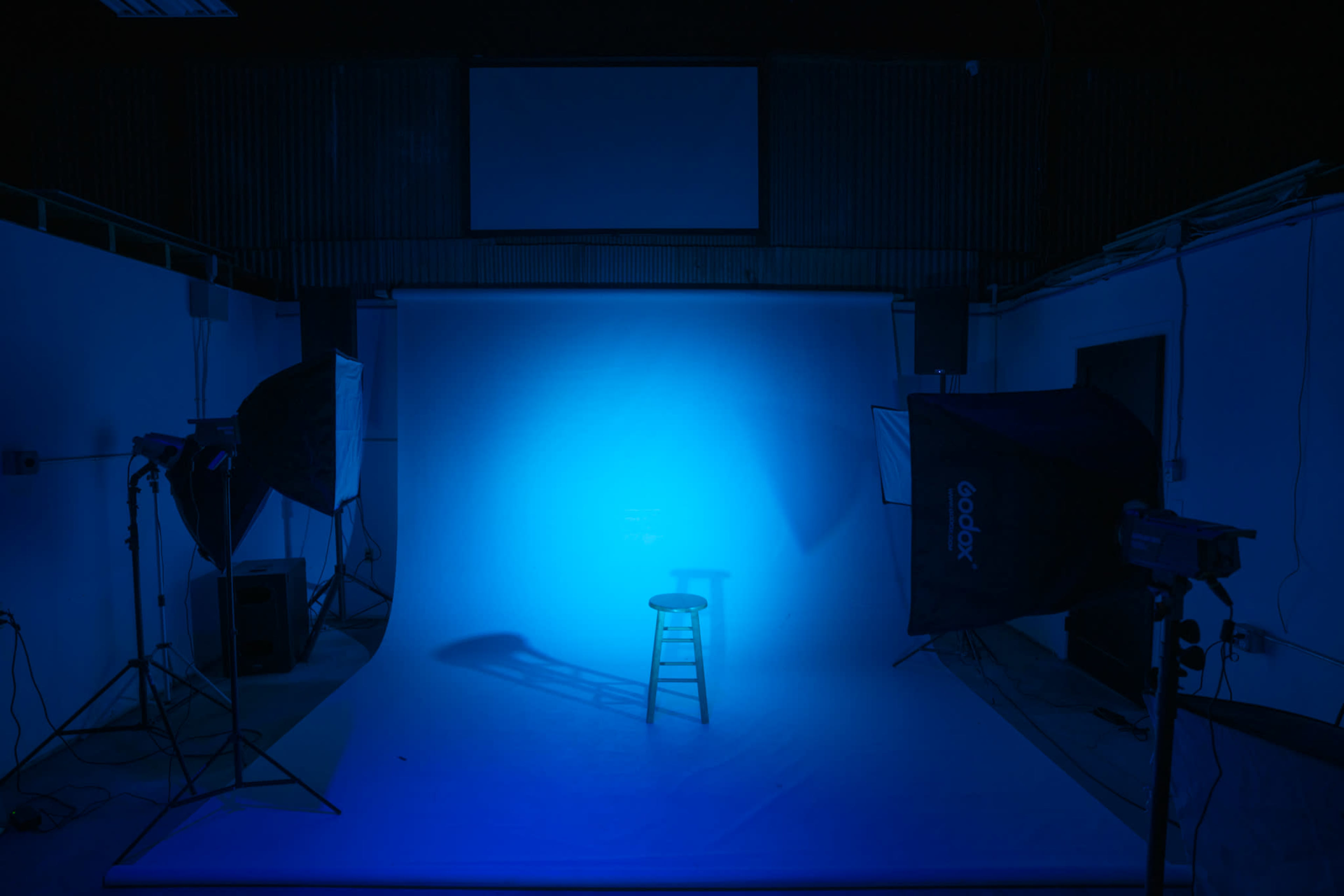 A single wooden stool is illuminated on a blue backdrop in a photography studio.