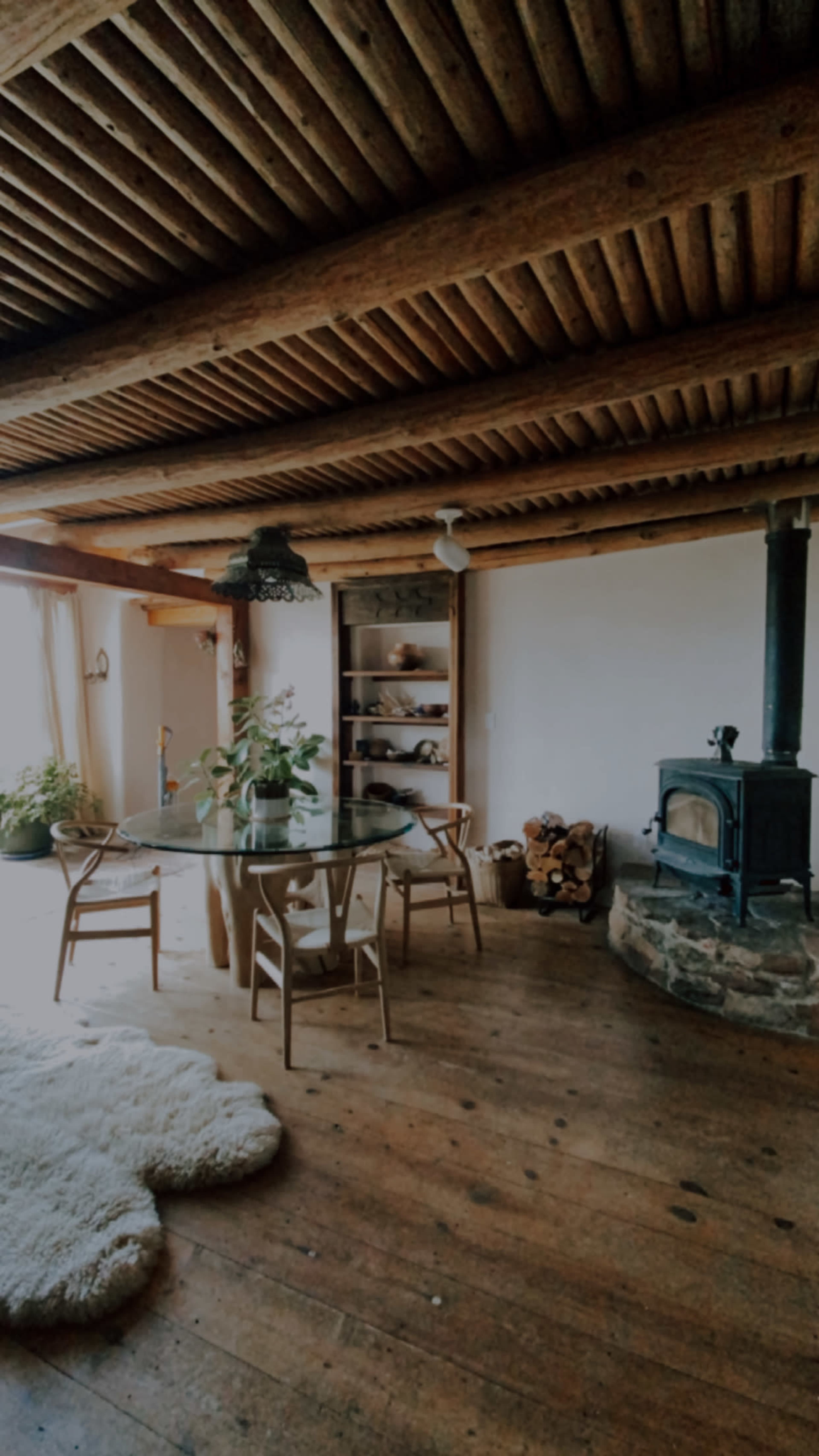 A wooden dining area with a round glass table, four chairs, a stone fireplace, and shelves along one wall.