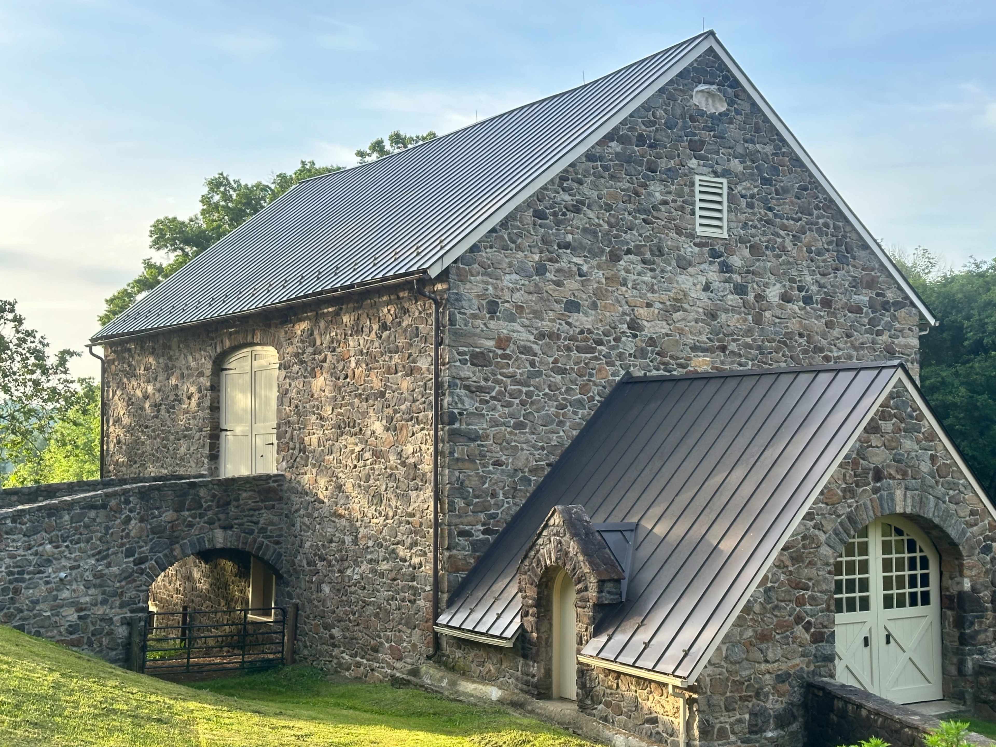 A stone building with a metal roof, featuring a large arched entrance and a grassy area in front.