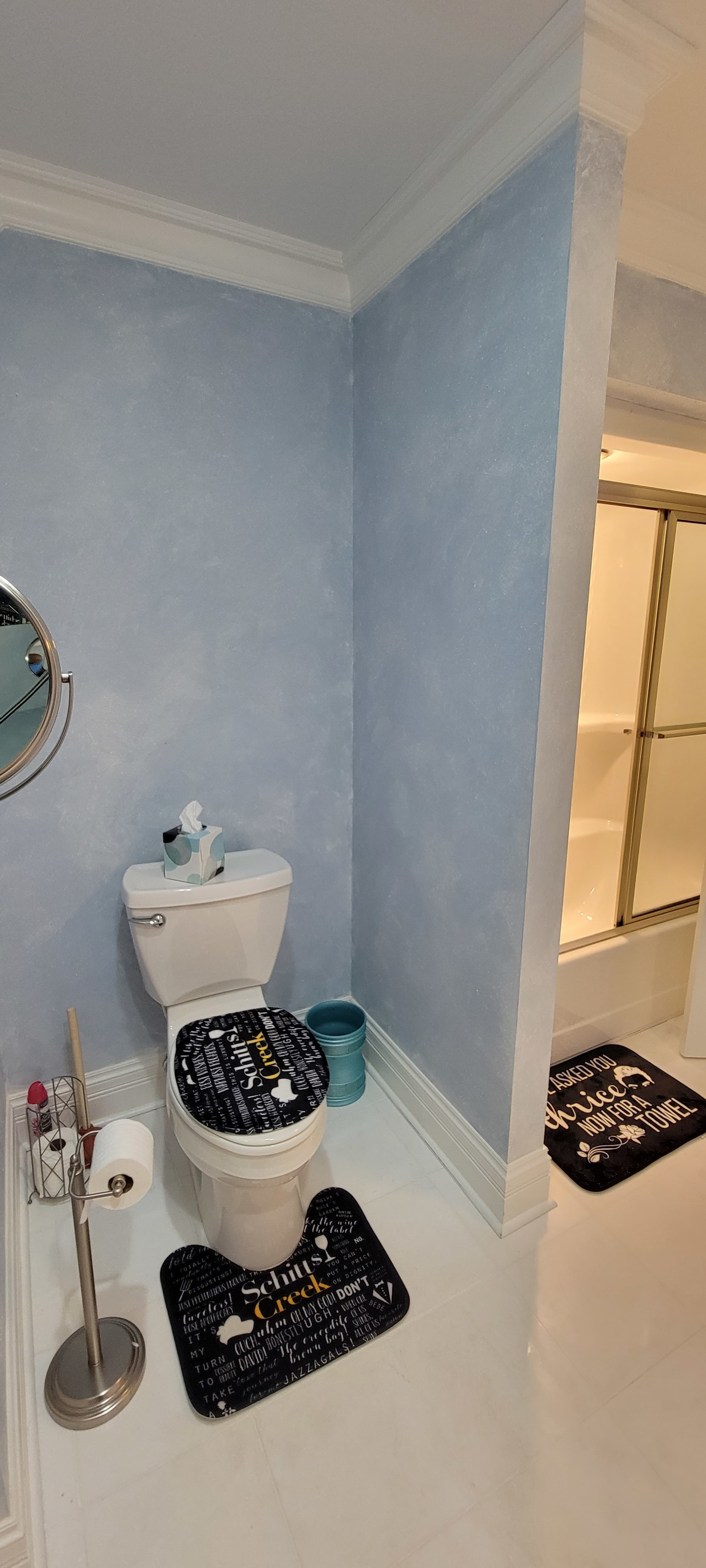 A bathroom with a white toilet, two black and gold bath mats, and a shower area with a glass sliding door.