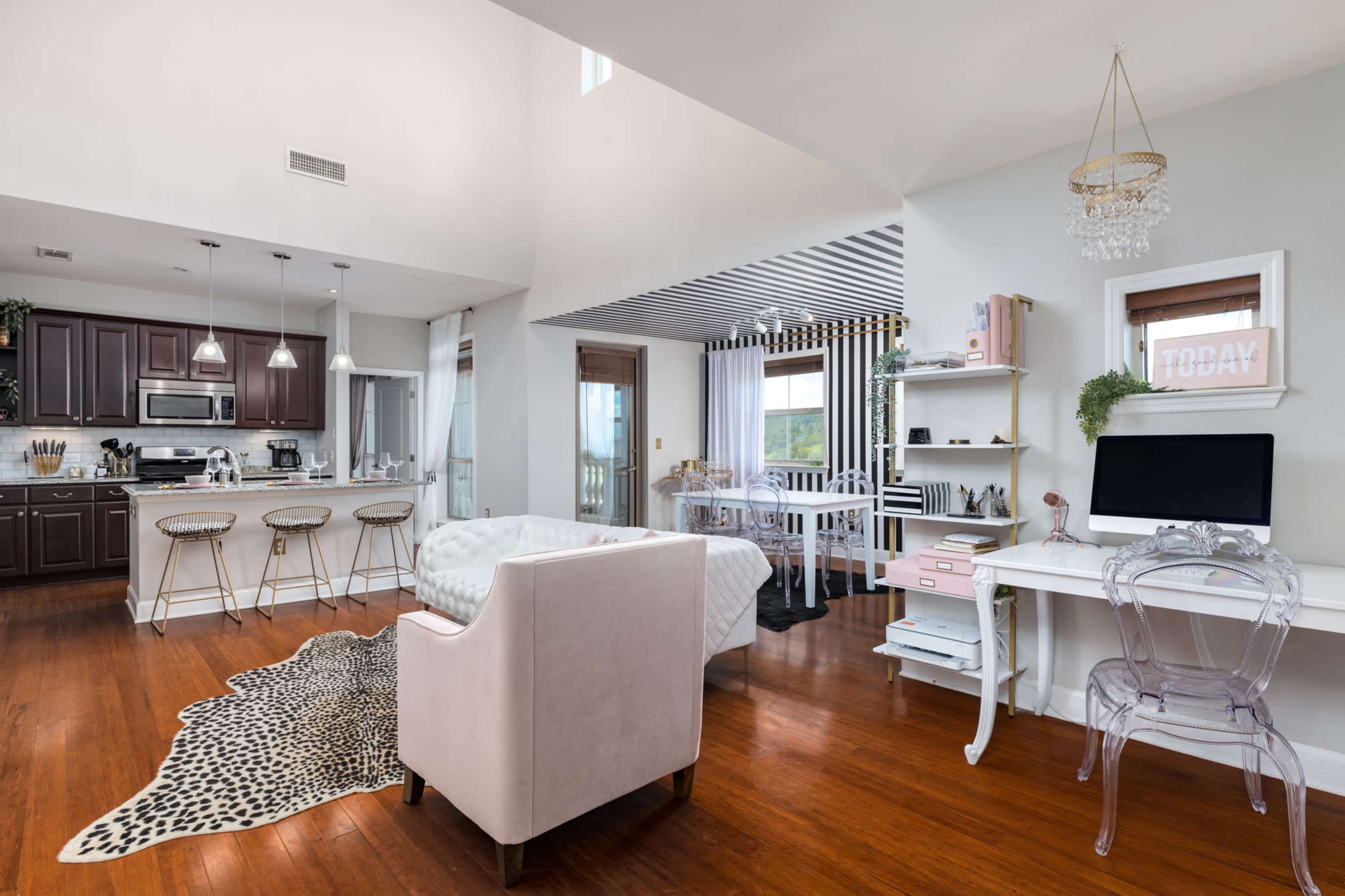 The image shows a modern living space featuring a kitchen area, a dining setup, and a cozy seating arrangement with wooden flooring.