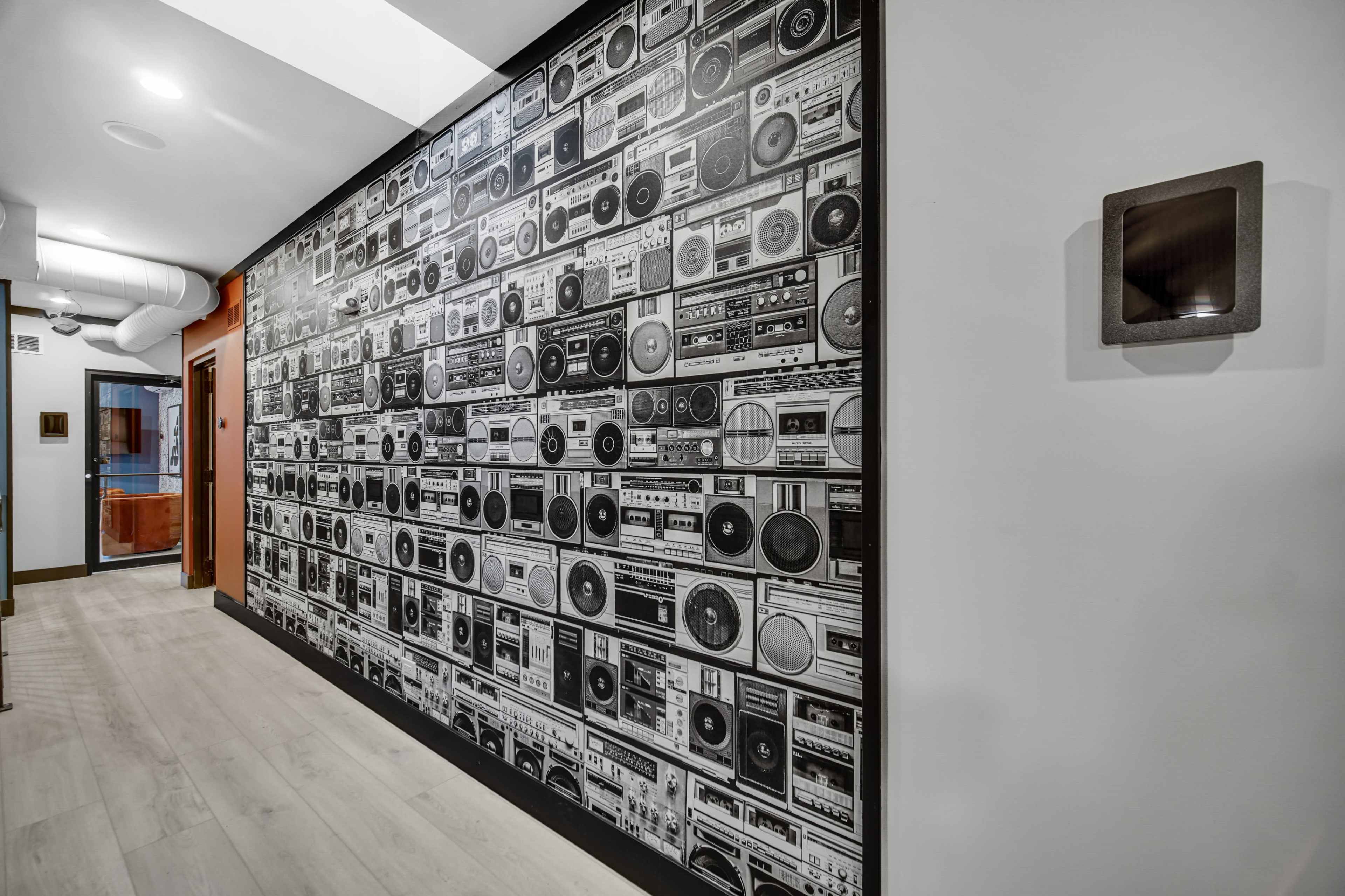 The image shows a hallway featuring a wall covered with a design of vintage audio cassette players and radios.