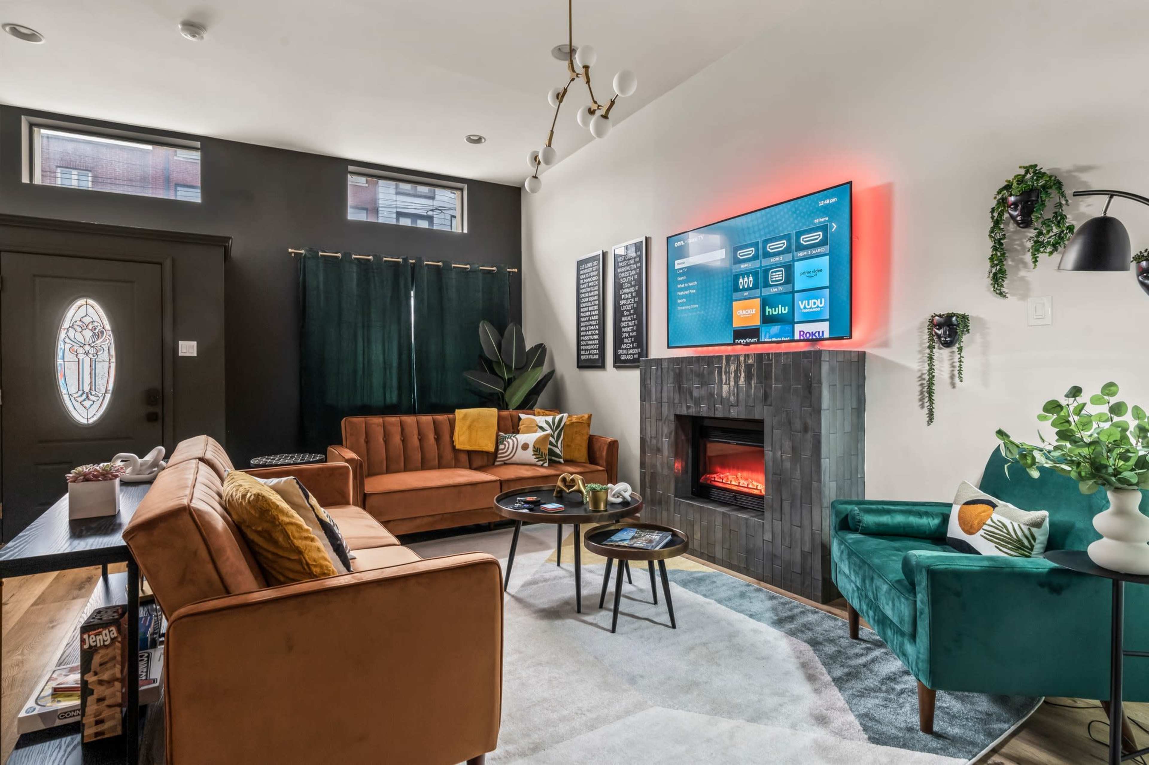 The living room features two sofas, a modern TV mounted on the wall, and a fireplace with a stone facade.
