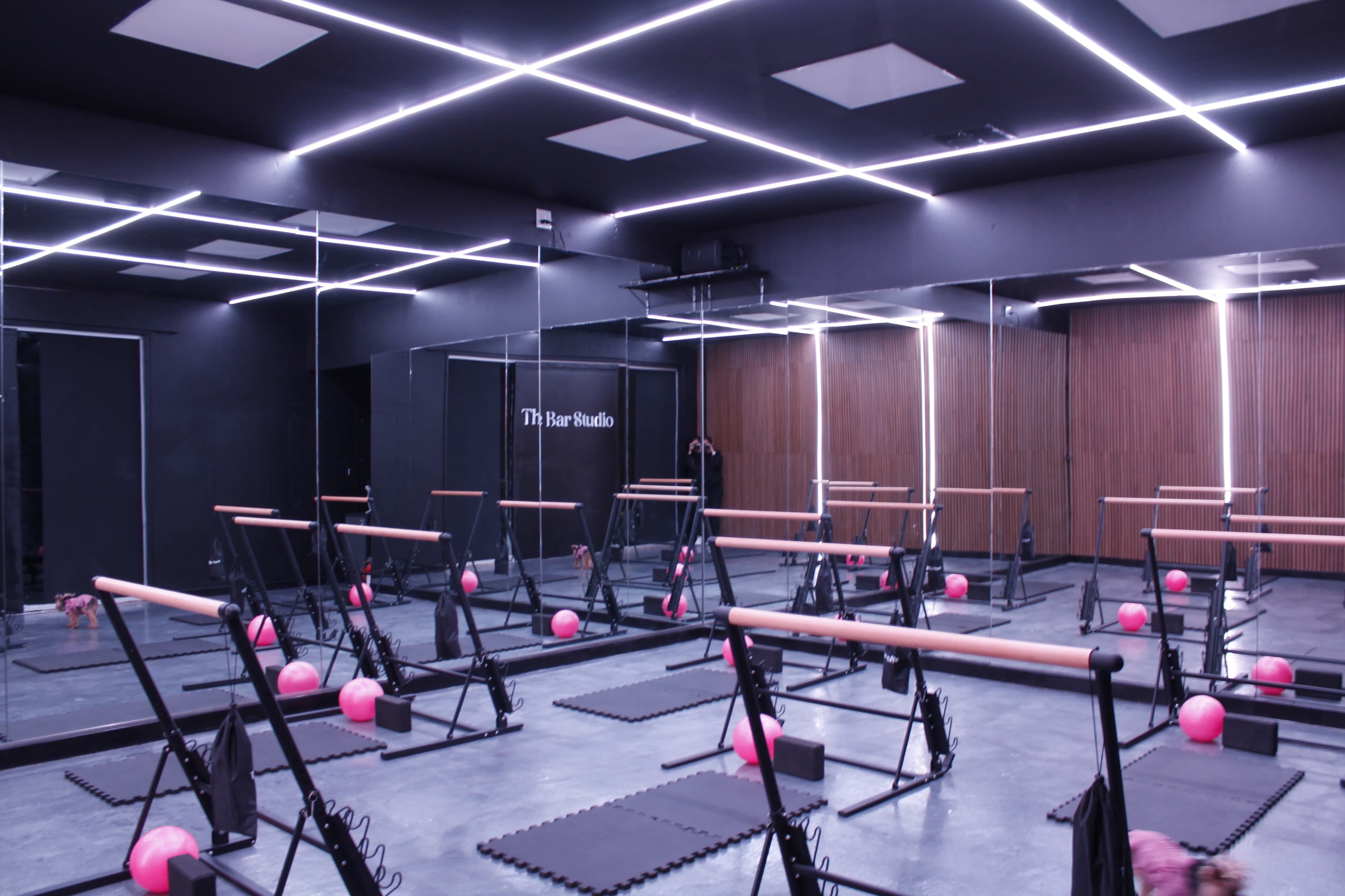 A mirrored fitness studio equipped with reformer machines and pink fitness balls arranged neatly on a gray floor.