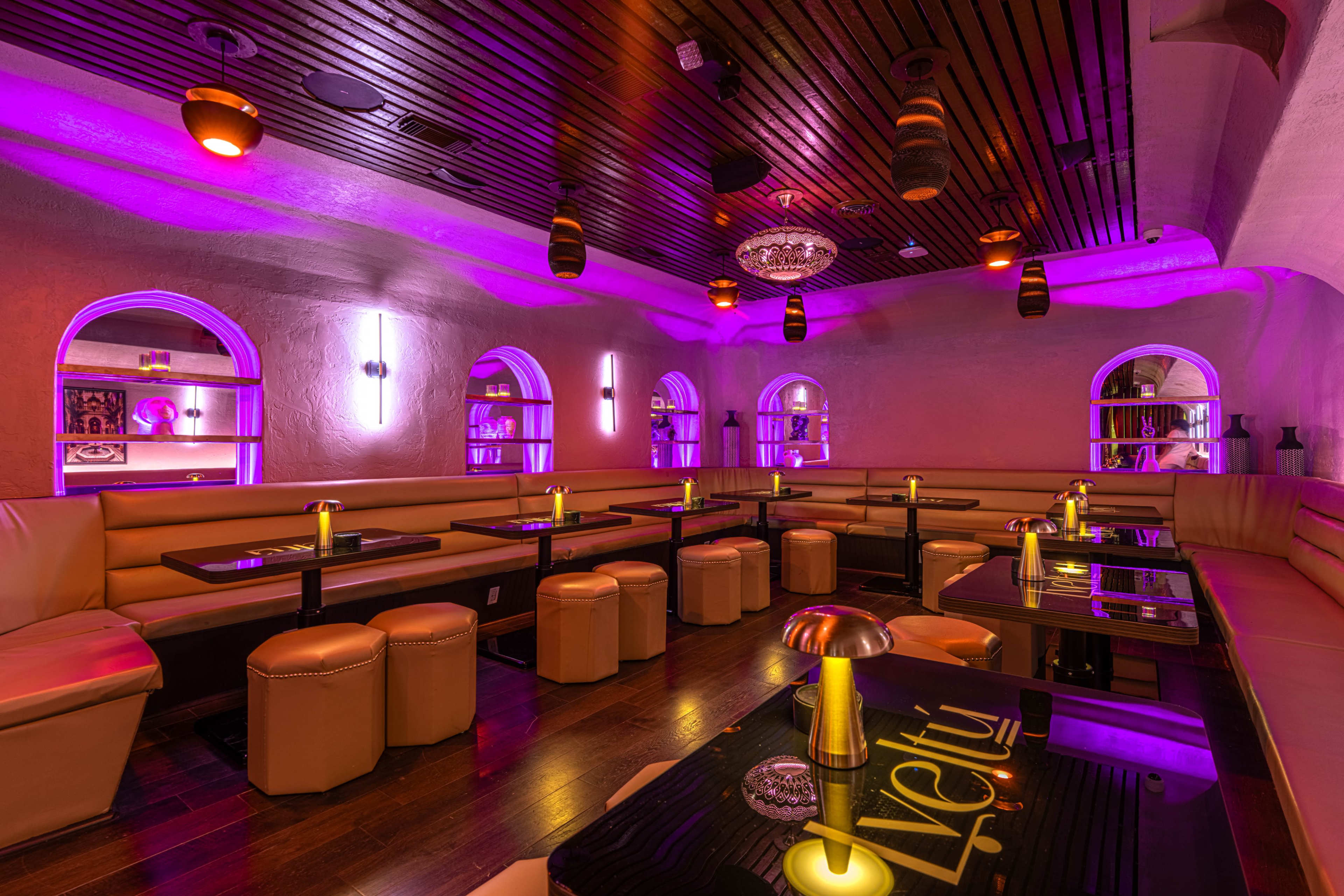 The image shows a dimly lit lounge with purple lighting, featuring plush seating areas, low tables, and decorative elements.