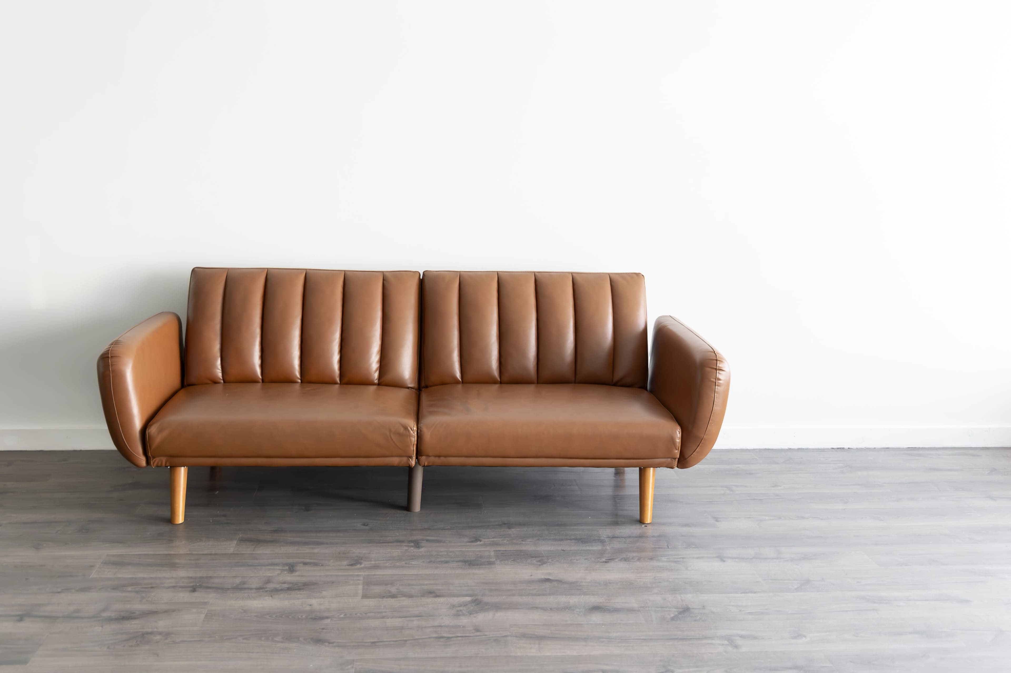 A brown leather sofa with vertical stitching is positioned against a plain white wall.
