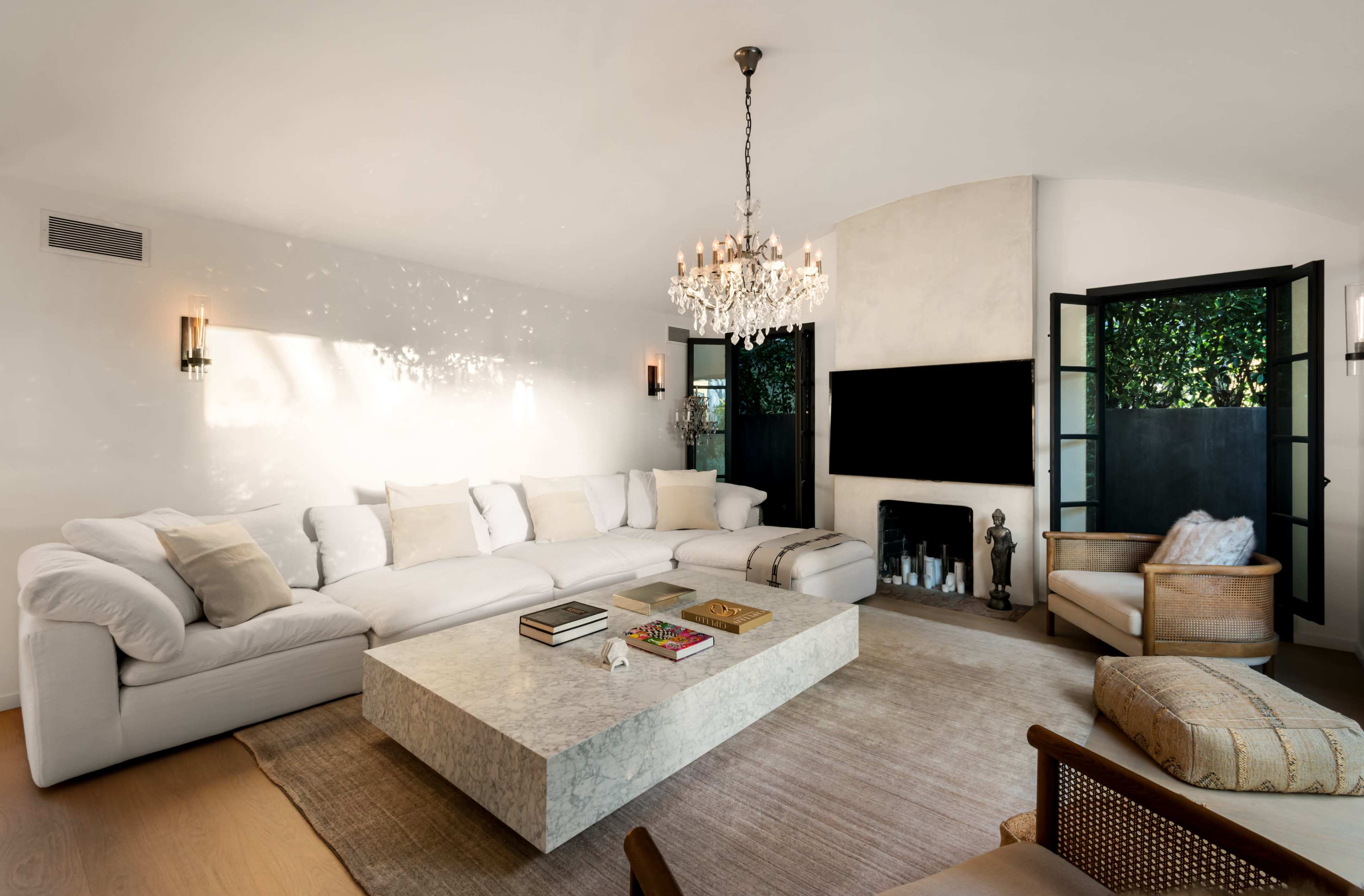 The living room features a large white sofa, a marble coffee table, and a fireplace, with an elegant chandelier hanging from the ceiling.