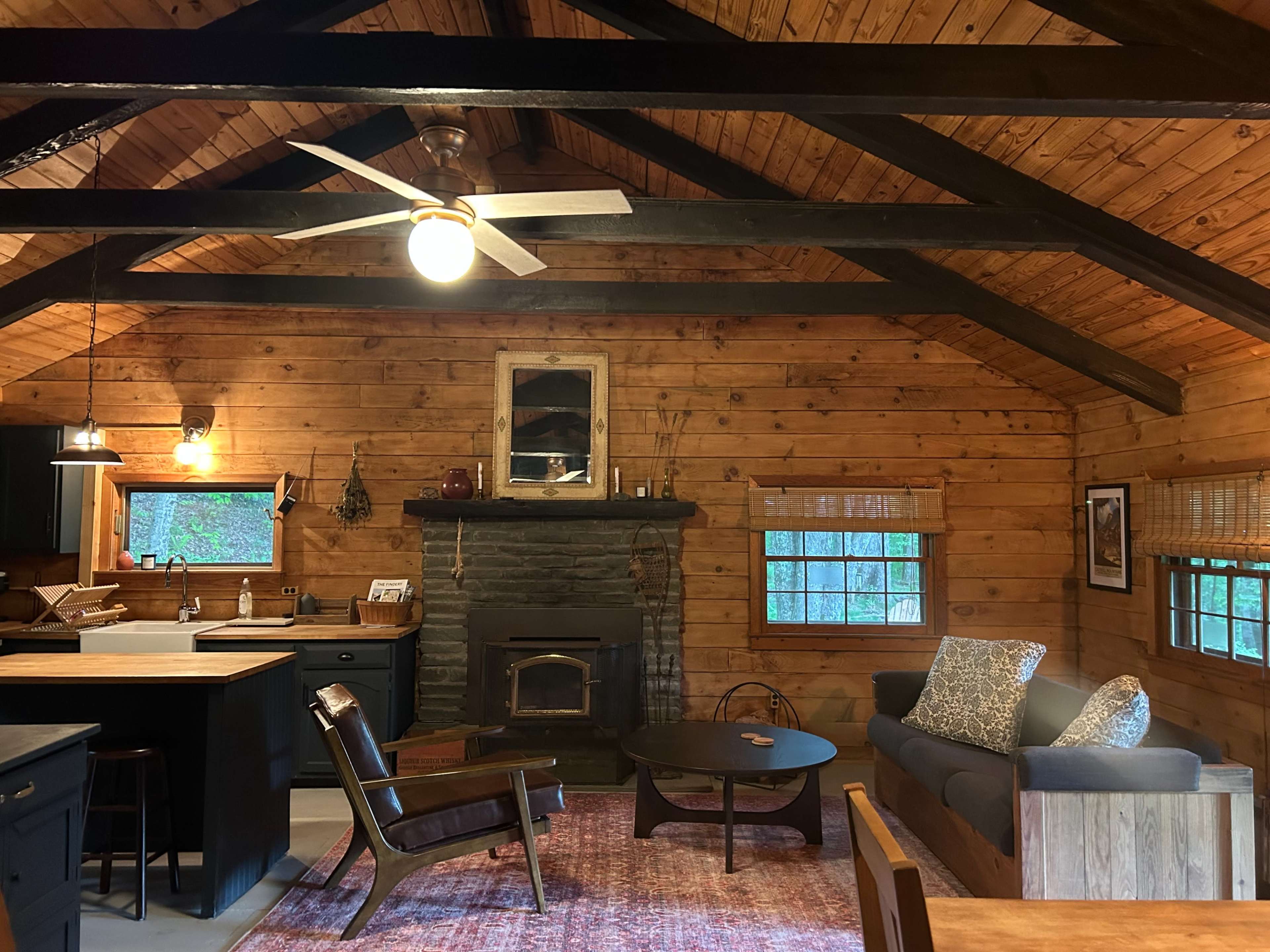 The image shows a warm, wooden cabin interior with a living area featuring a couch, a coffee table, and a stone fireplace.