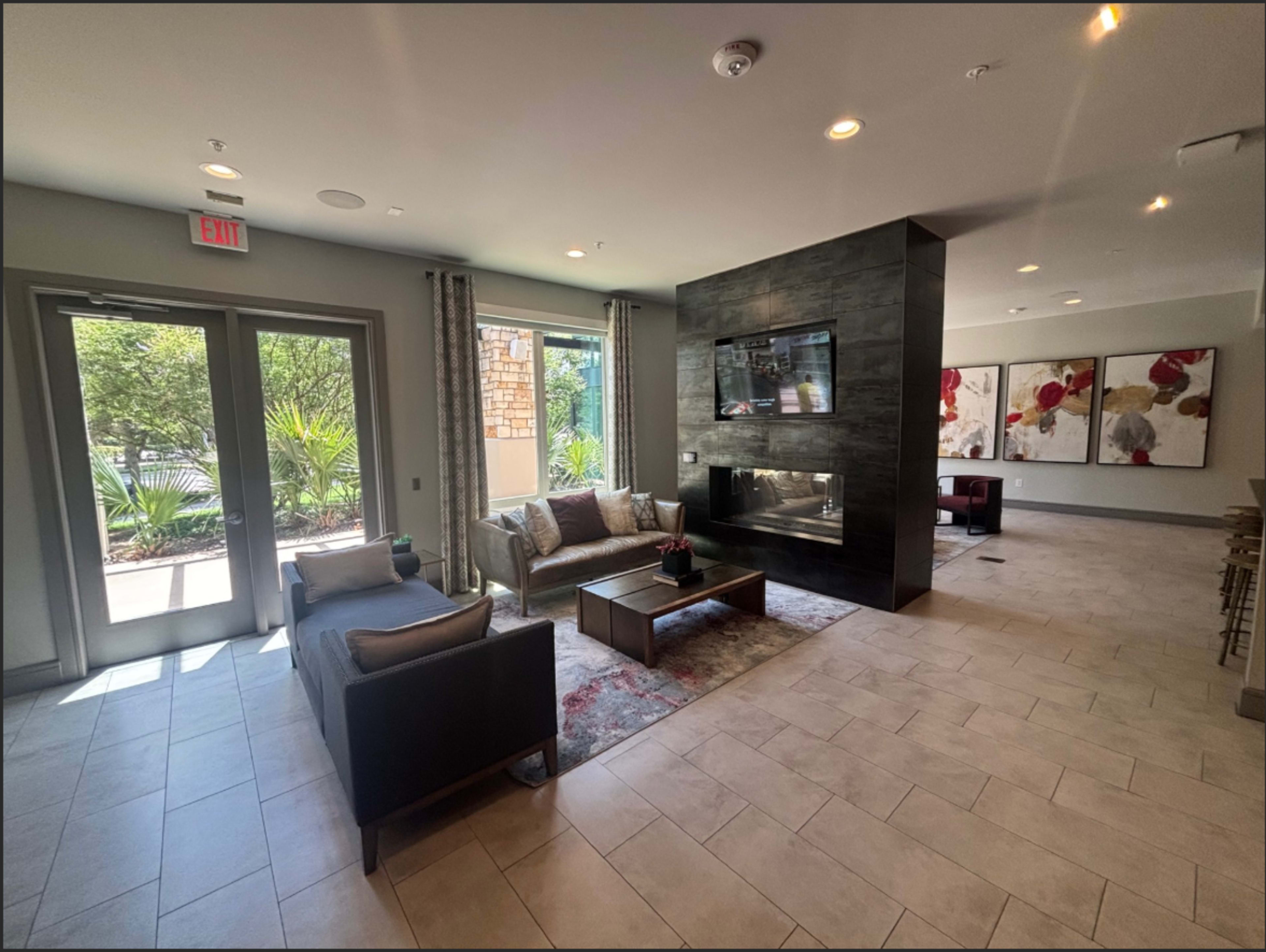The image shows a modern lounge area with a seating arrangement, a fireplace, and large windows providing natural light.
