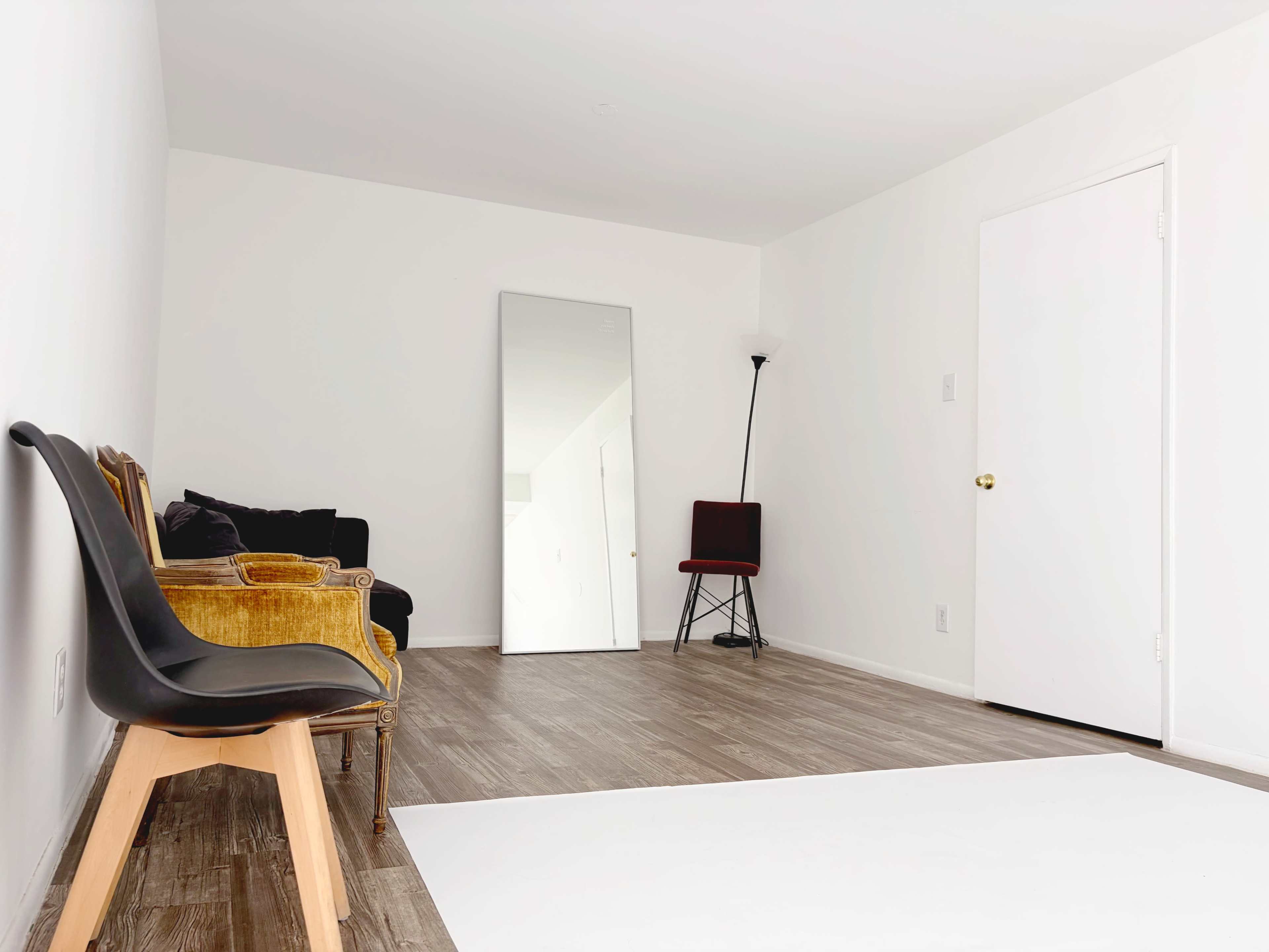 The room features a minimalistic design with a large mirror, two chairs, a lamp, and a white wall.