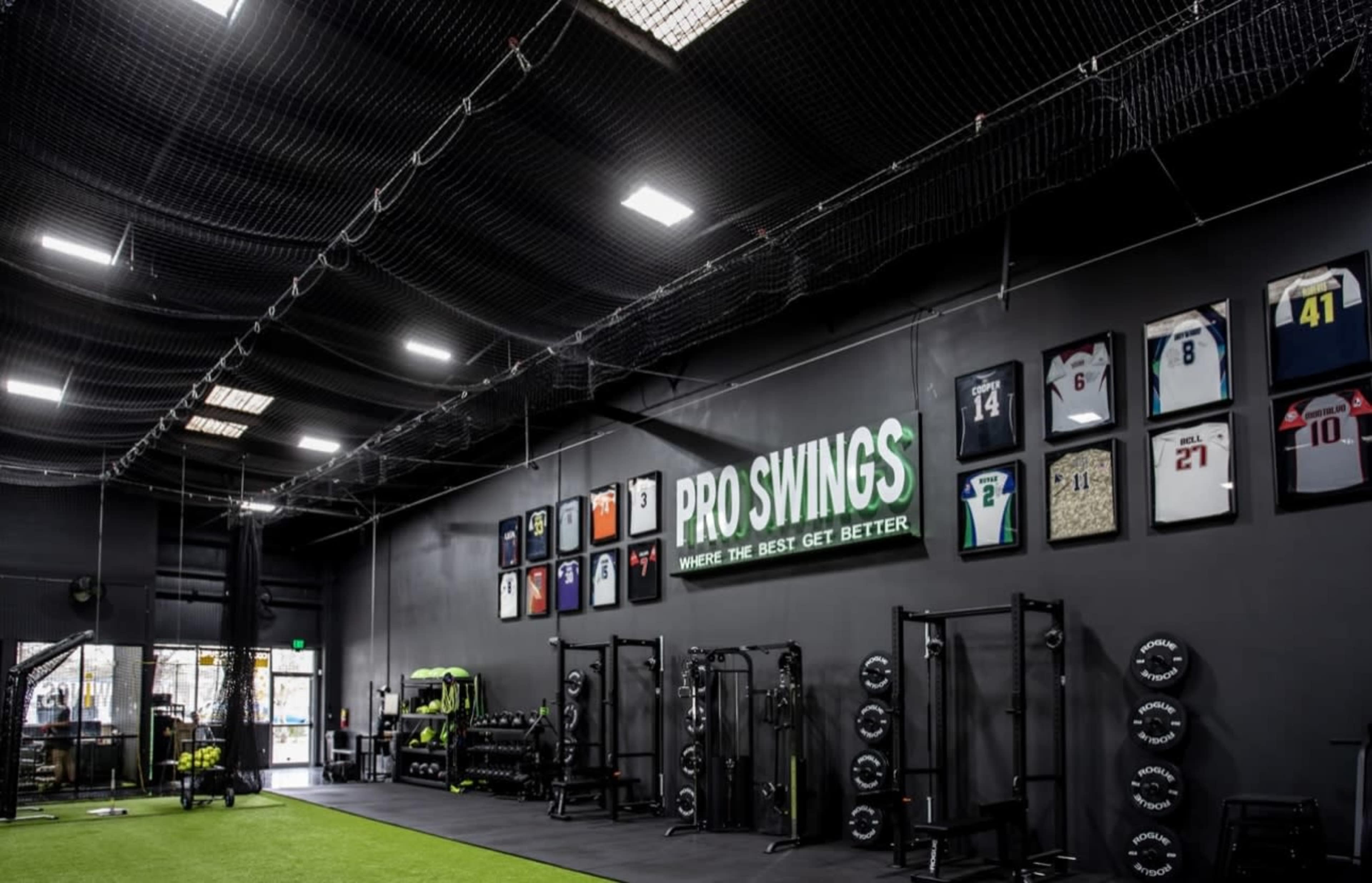 The image shows a gym interior with a green turf floor, weightlifting equipment, and framed jerseys displayed on the wall.