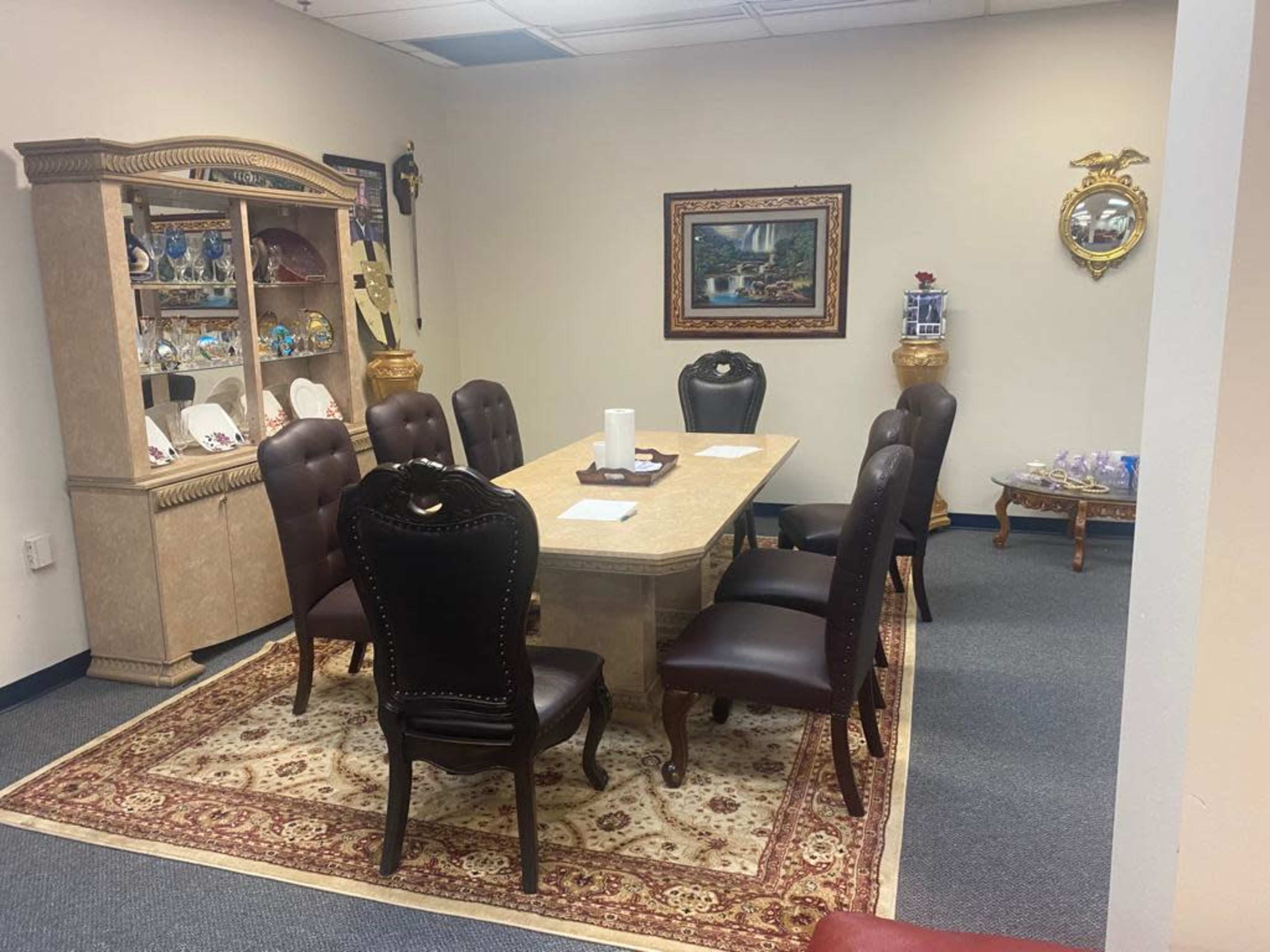 A conference room with a large table surrounded by eight leather chairs, a display cabinet, and decorative wall art.