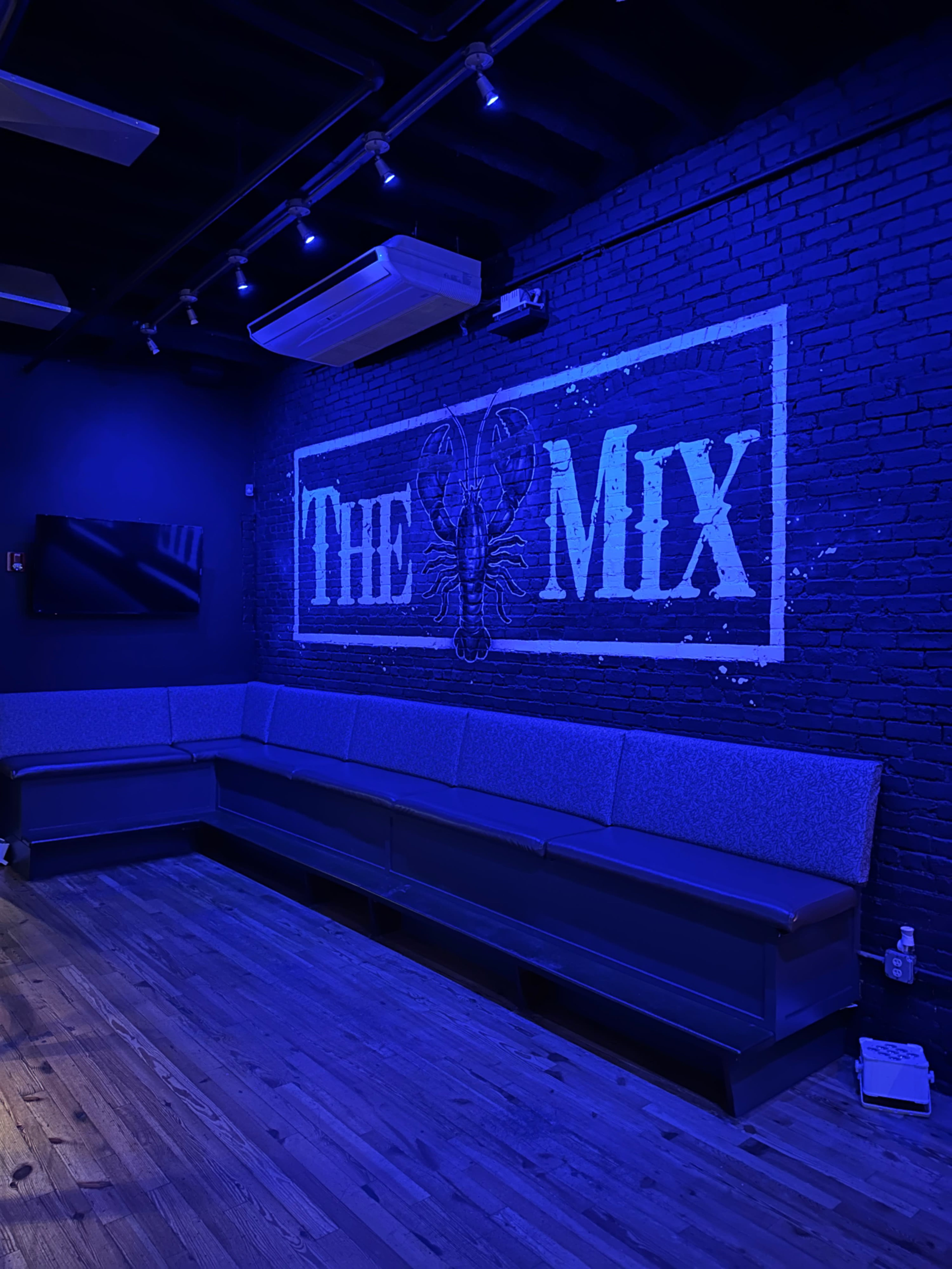 A dimly lit lounge area with a large blue mural reading "THE MIX" on a black brick wall and a long gray couch along the side.