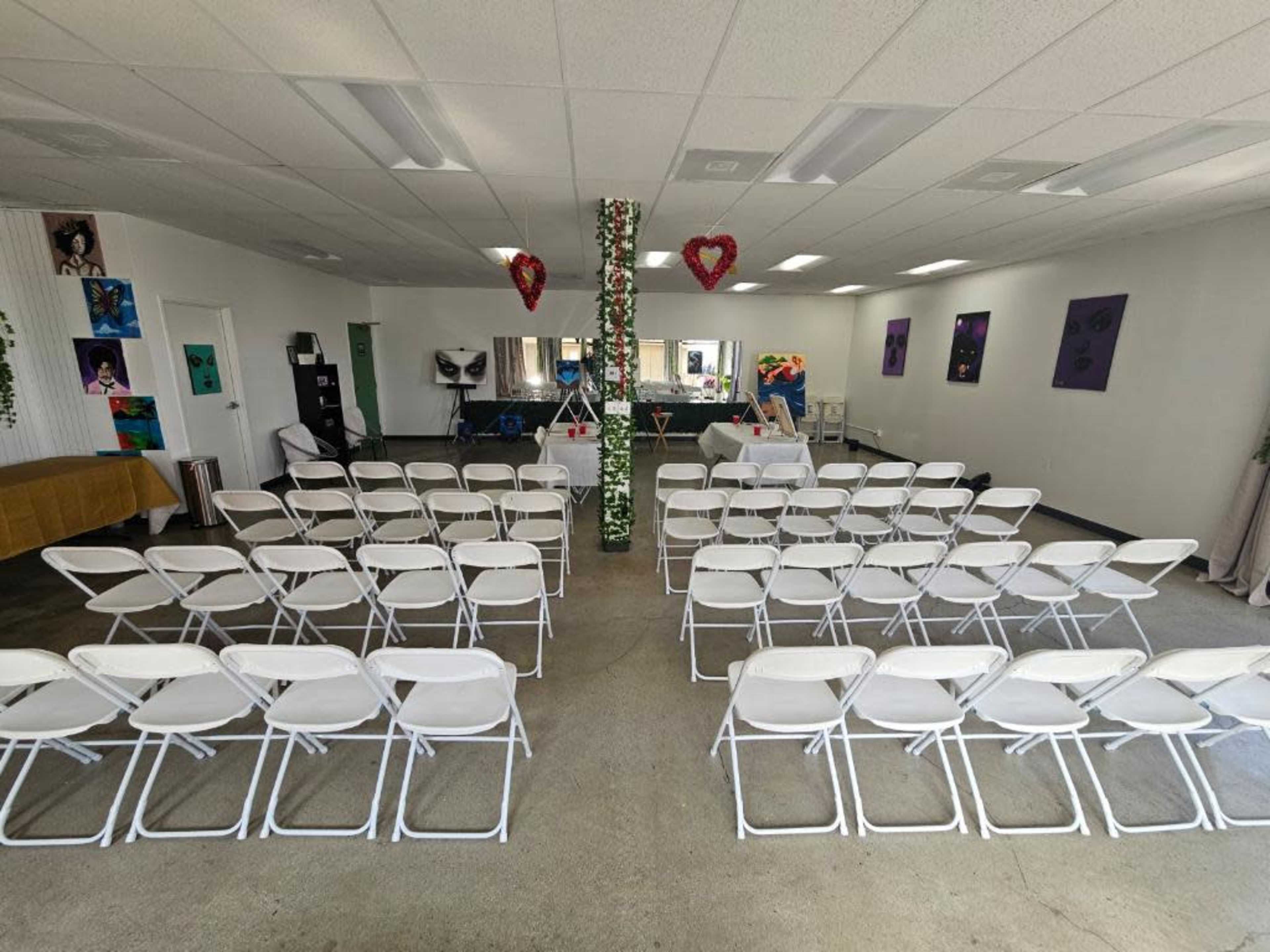 A large room set up with multiple rows of white folding chairs facing a central area adorned with decorations.