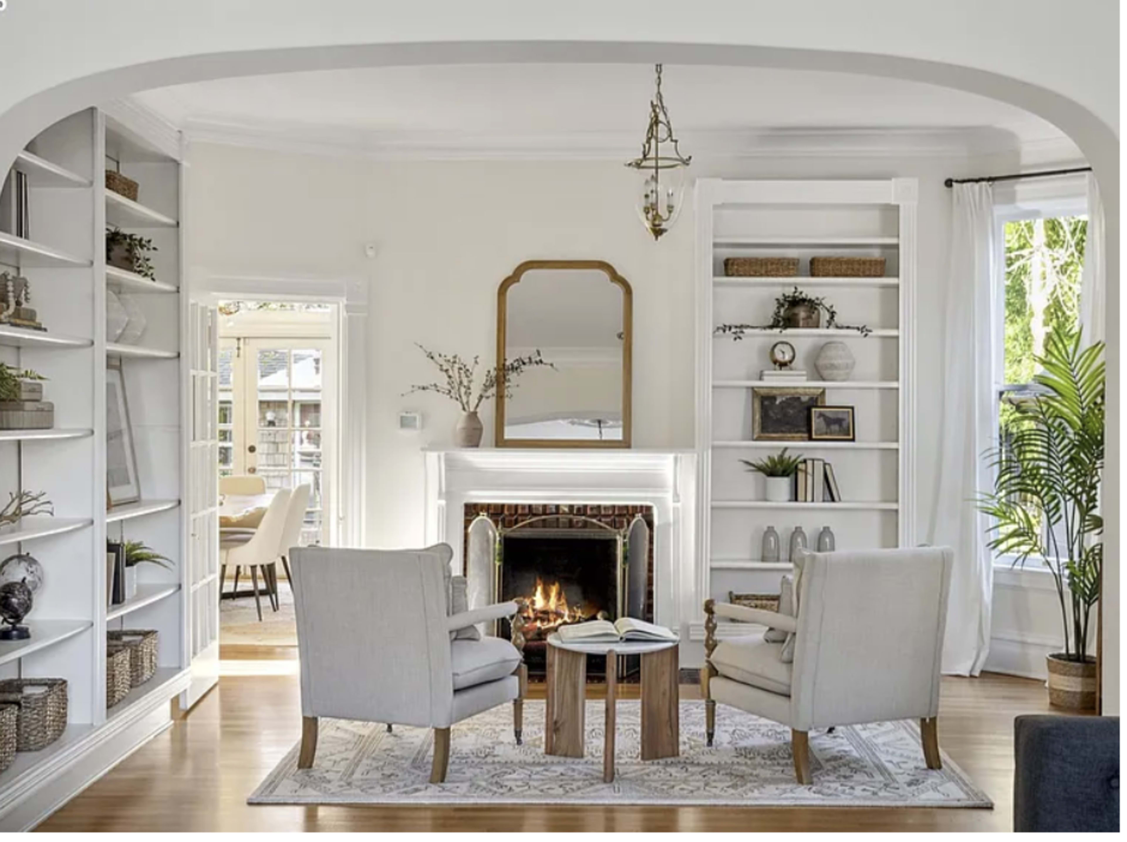 The image shows a cozy living room with two armchairs, a small wooden coffee table, a fireplace, and built-in bookshelves.