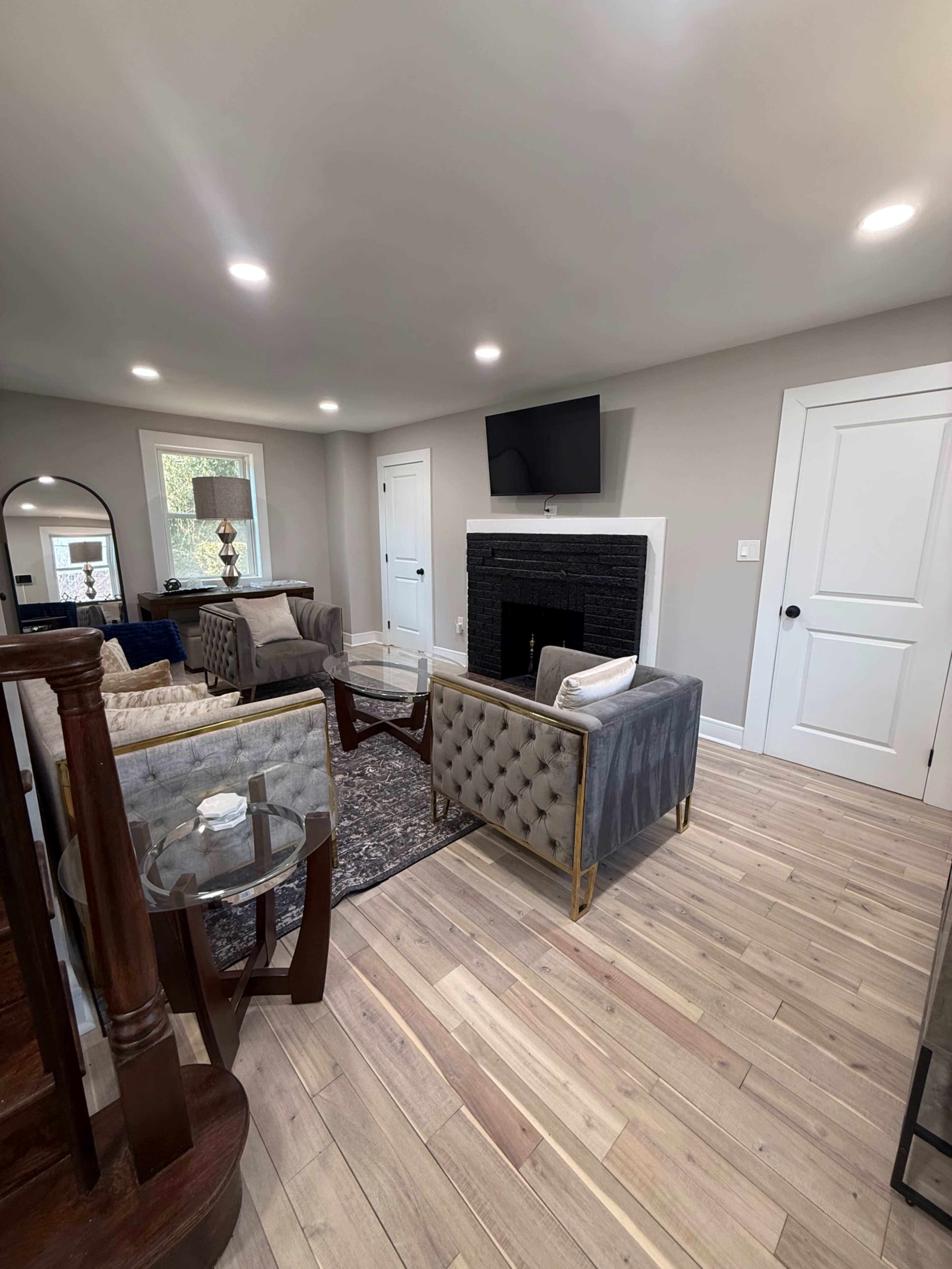 A modern living room features gray seating, a stone fireplace, a wall-mounted TV, and hardwood flooring.