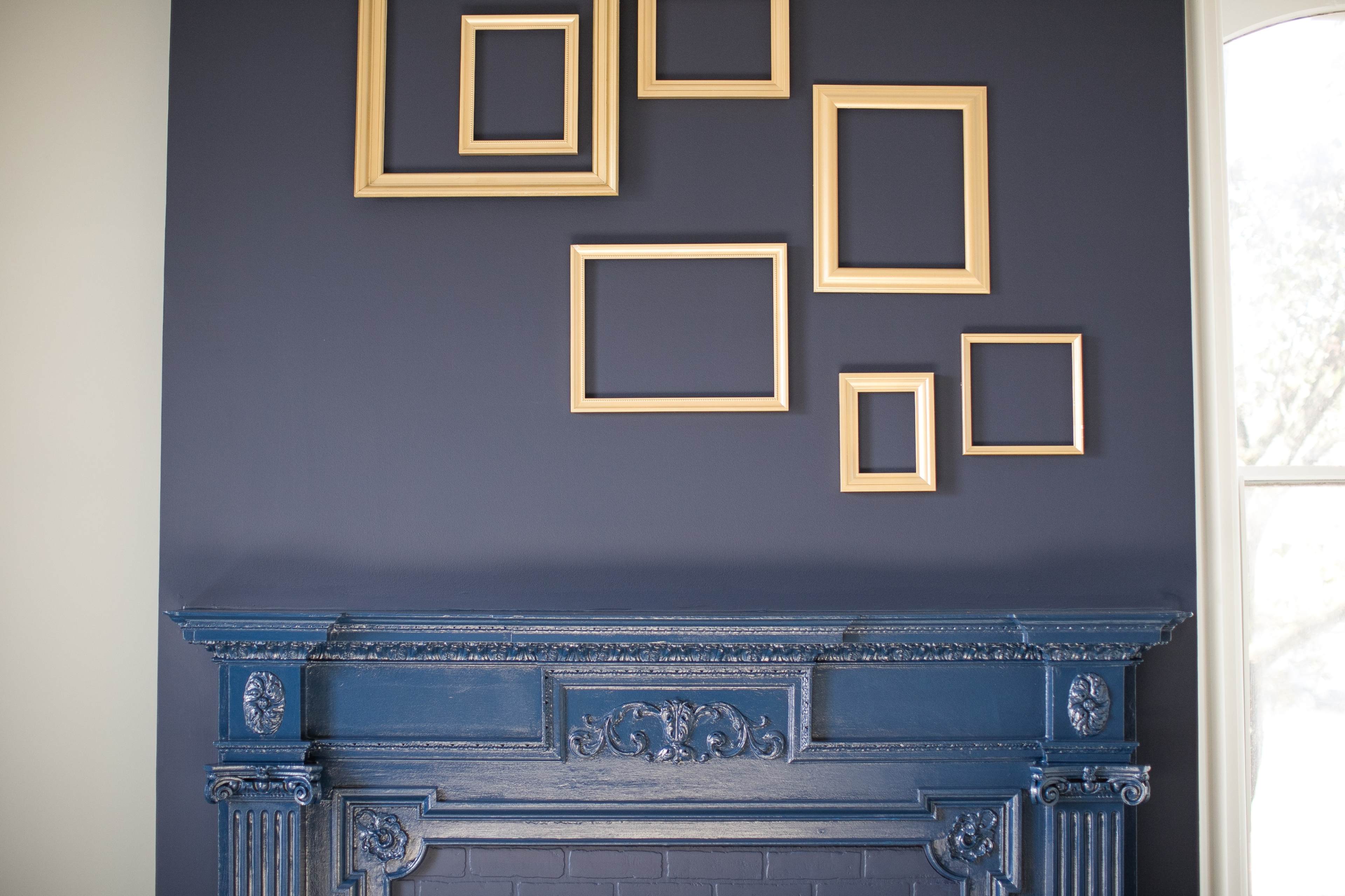A dark blue wall adorned with multiple gold-framed empty picture frames above an ornate blue fireplace.