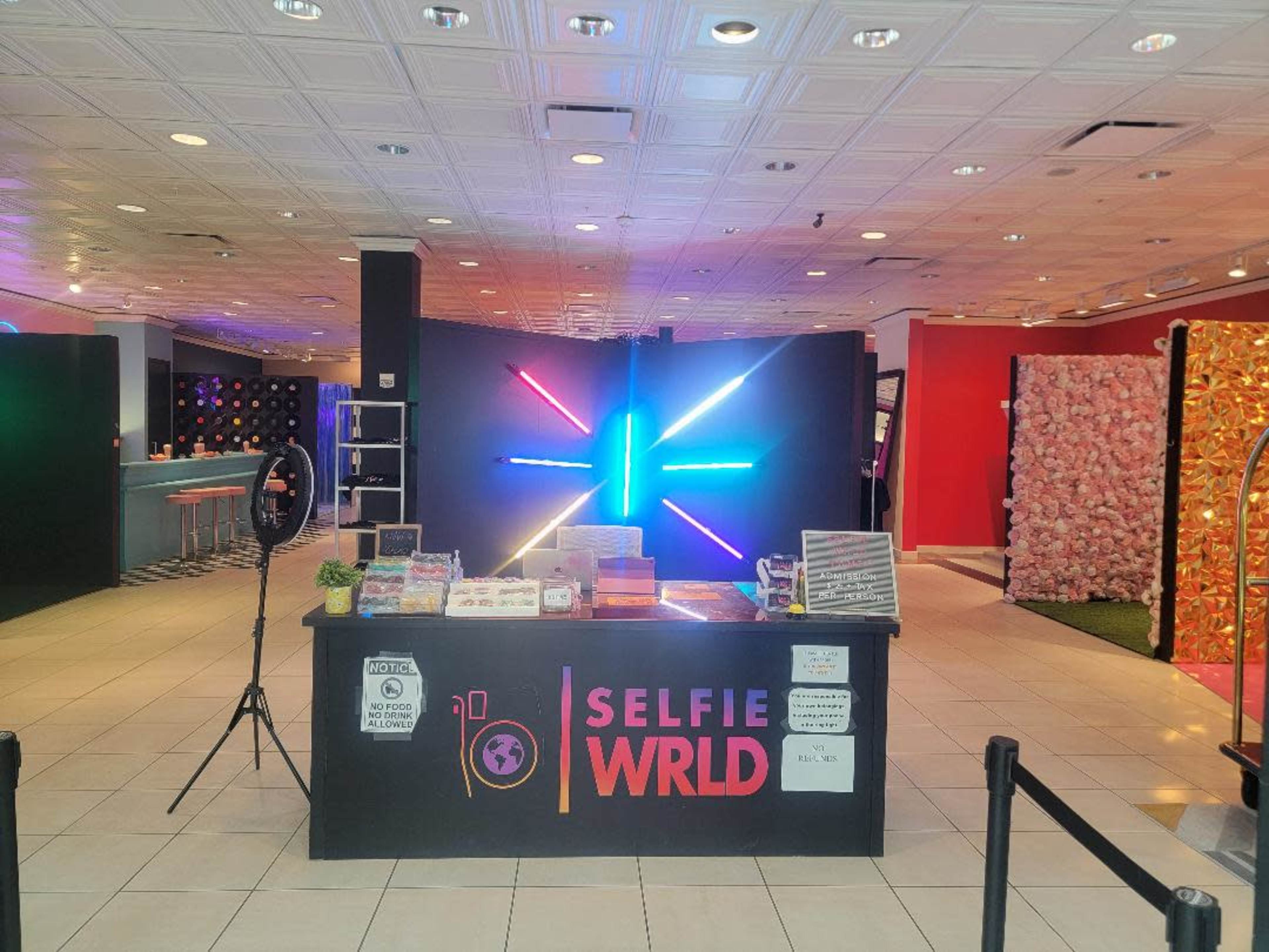A colorful selfie studio with a central counter labeled "SELFIE WRLD" and vibrant neon lights in the background.