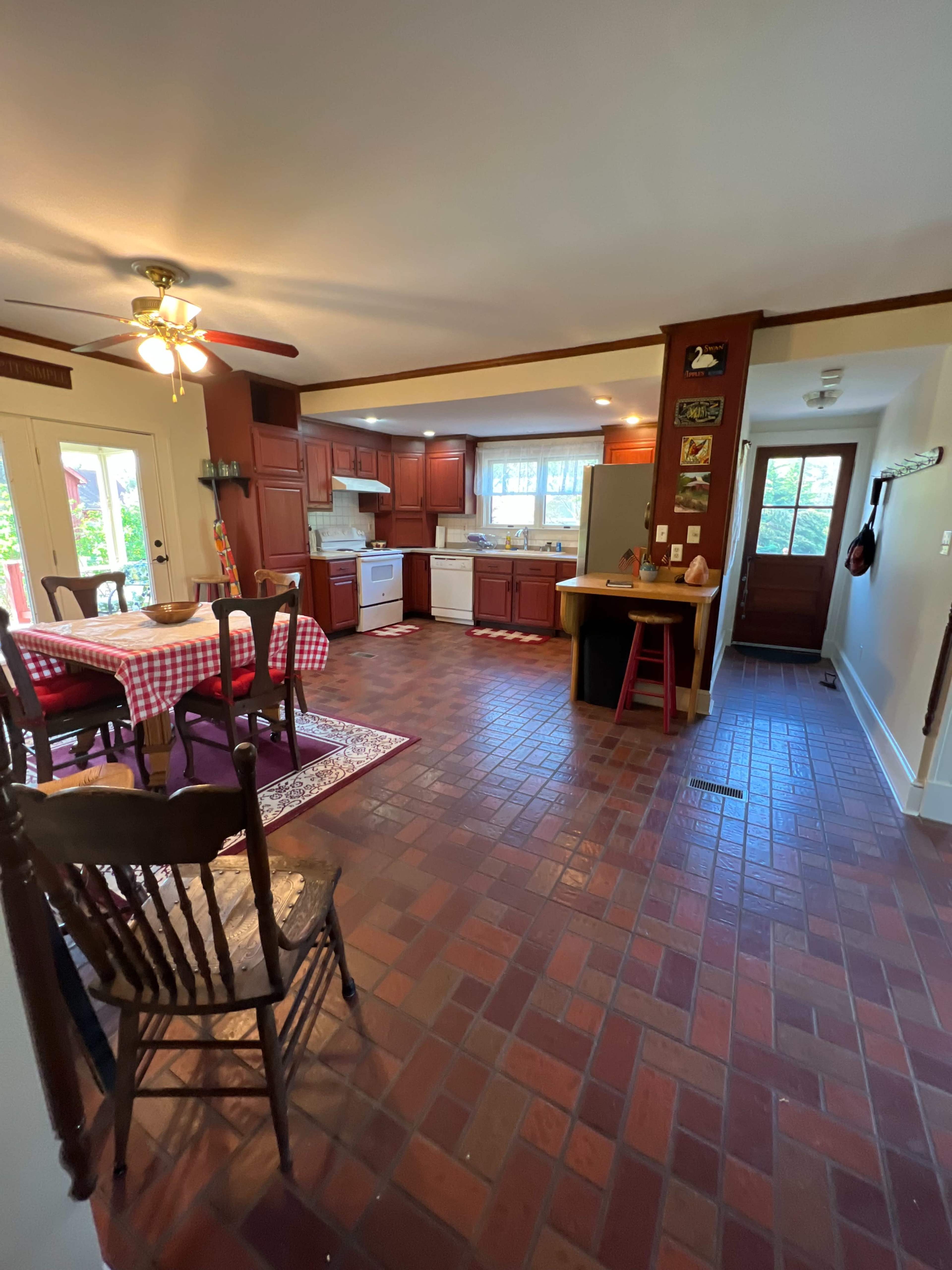 A spacious kitchen features wooden cabinets, a checkered tablecloth on a dining table, and a tile floor.