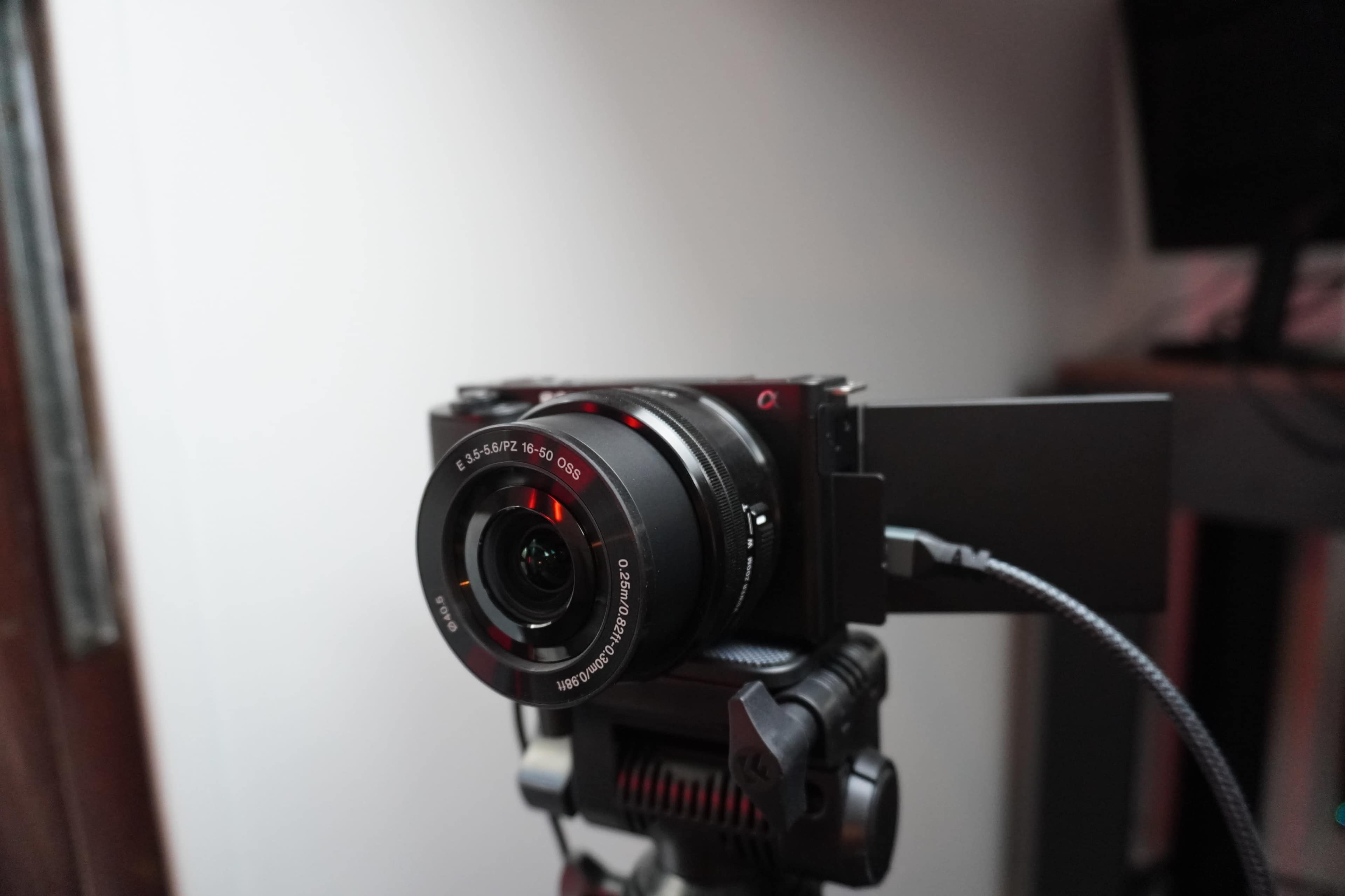 A camera is mounted on a tripod with a white wall in the background.