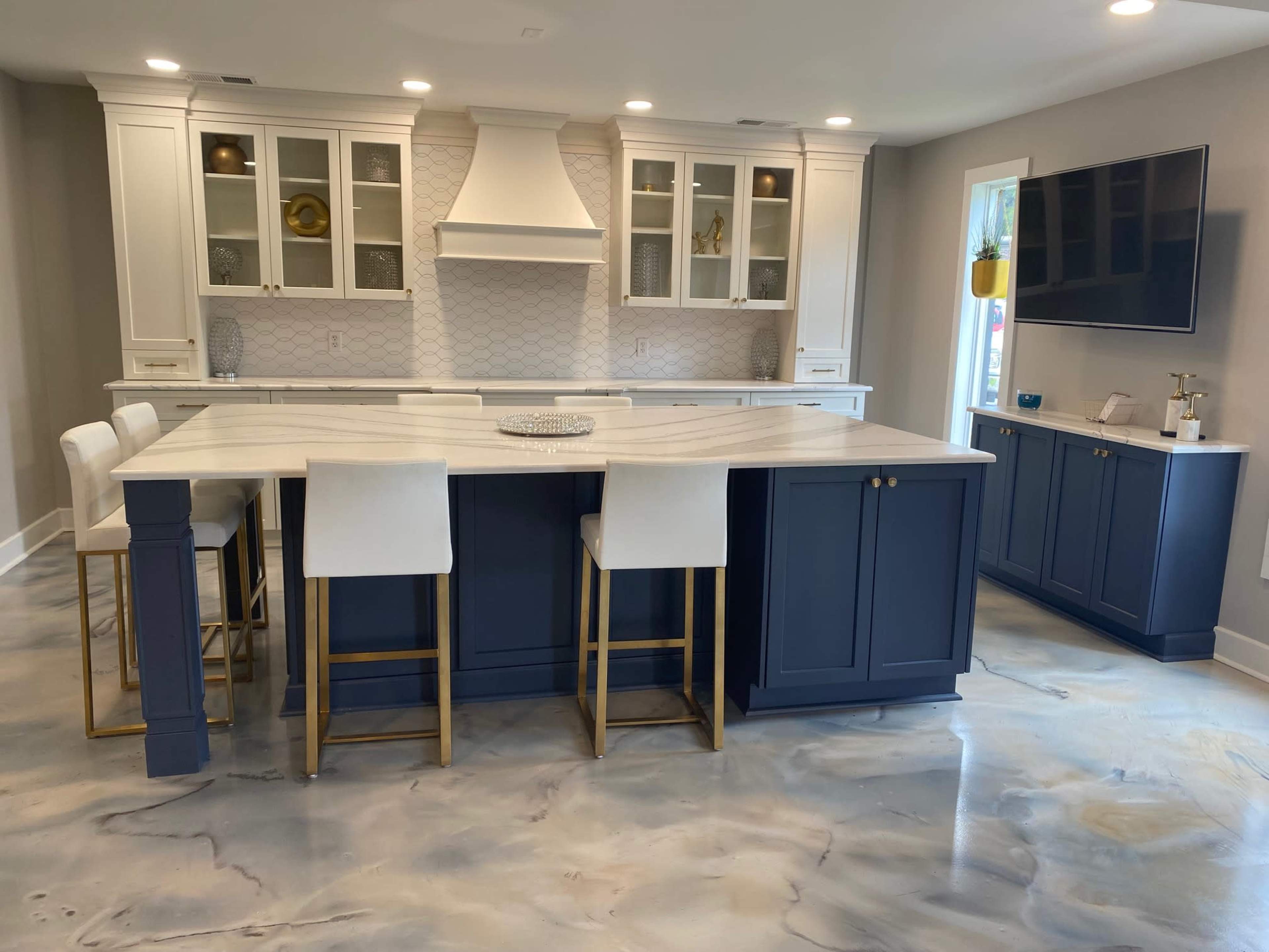 A modern kitchen featuring a large central island with white and gray marble countertops, navy blue cabinetry, and gold-accented bar stools.