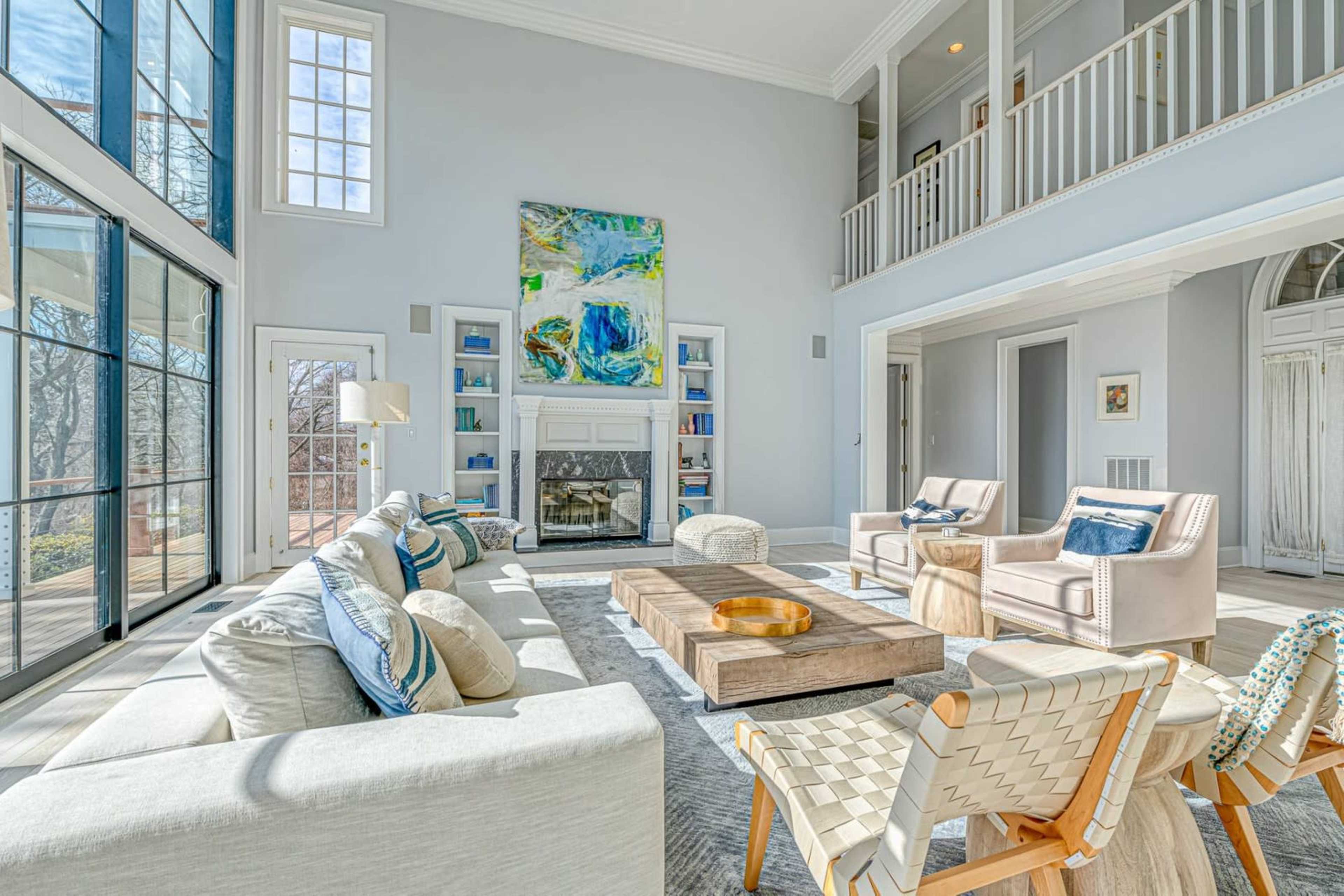 The bright living room features large windows, a contemporary fireplace, and a mix of comfortable seating arranged around a central wooden coffee table.