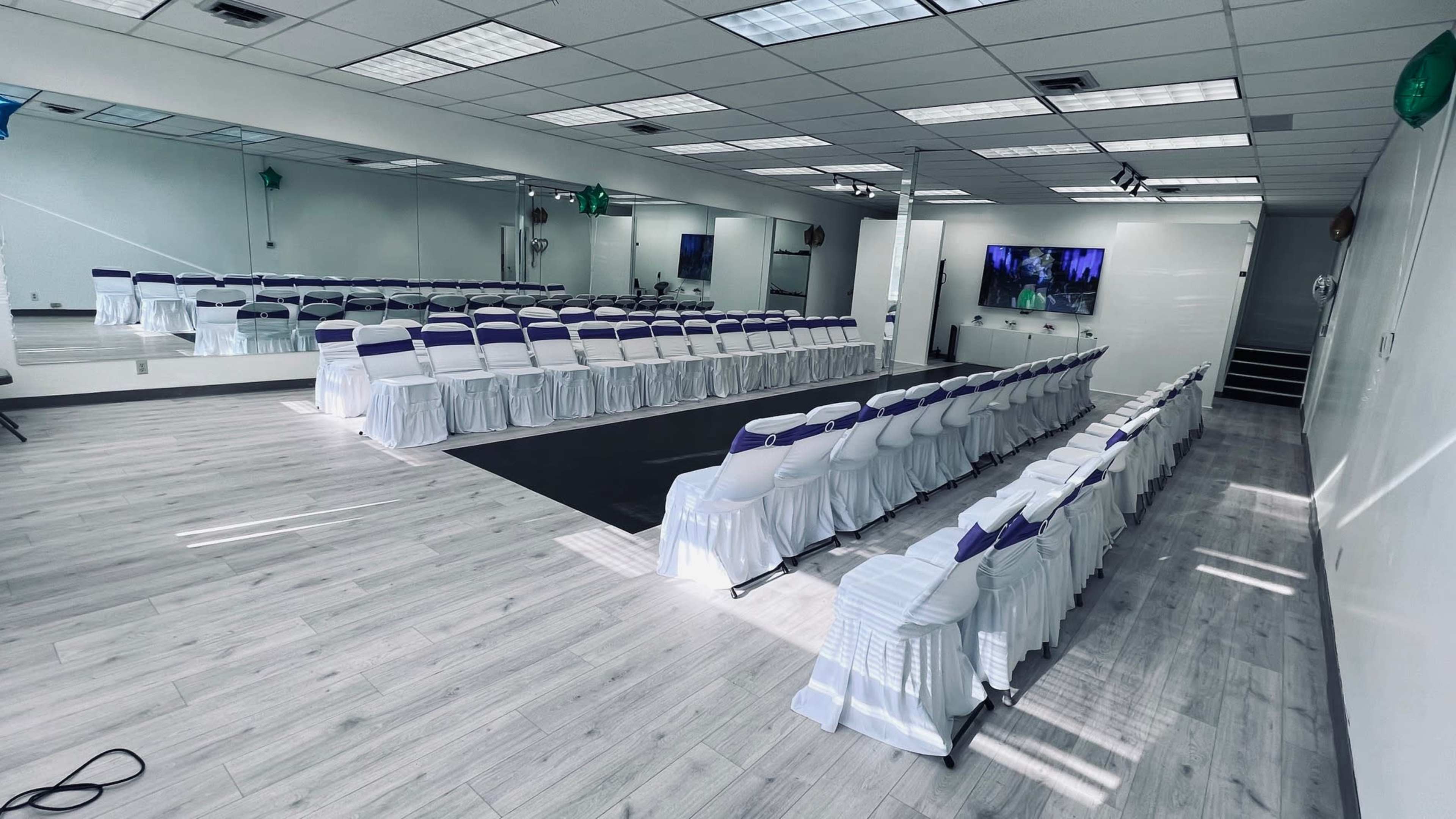 A well-arranged indoor event space with rows of chairs covered in white and purple, set up for a gathering.