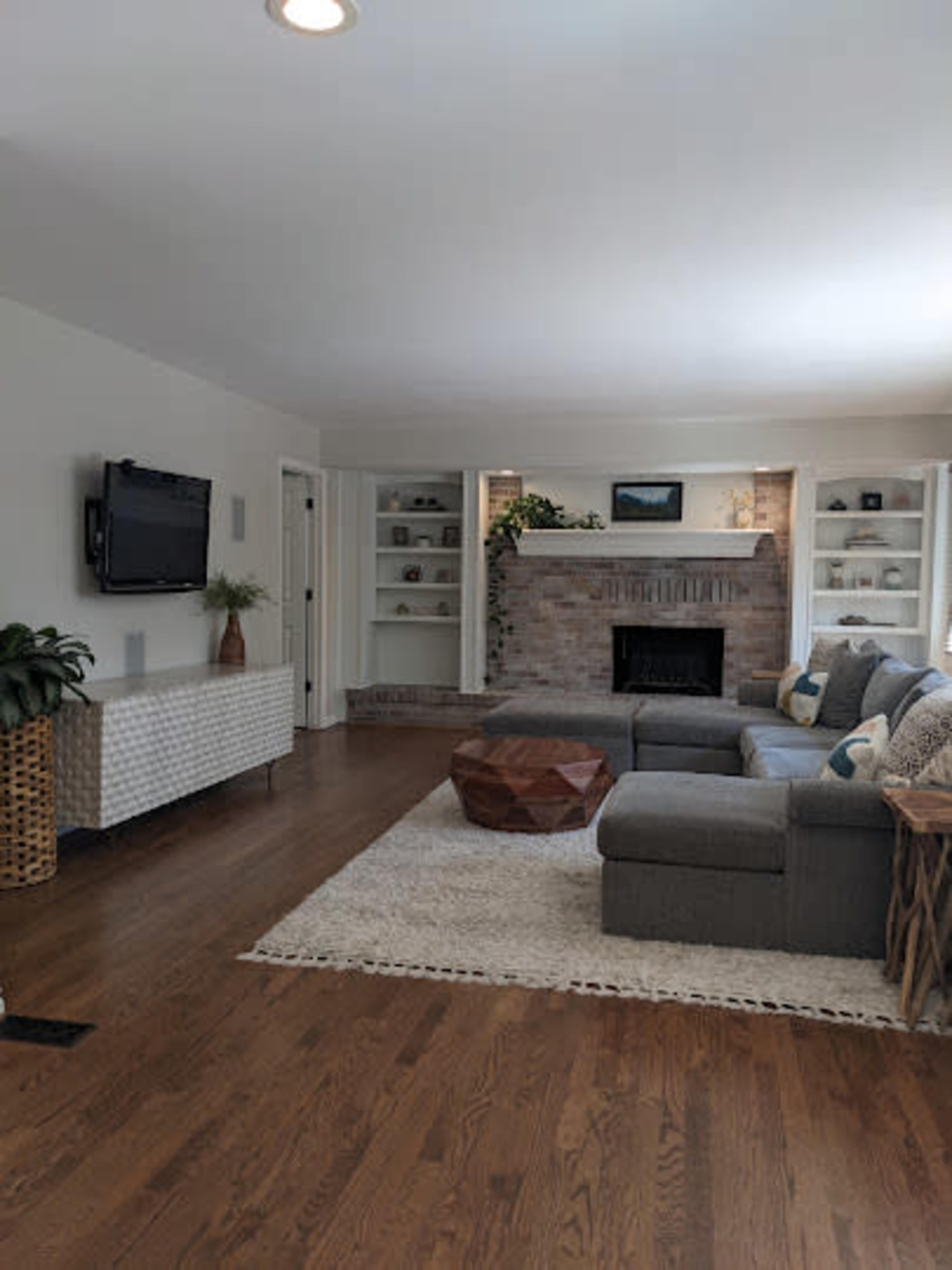 A modern living room features a gray sectional sofa, a wooden coffee table, and a brick fireplace with built-in shelves on either side.