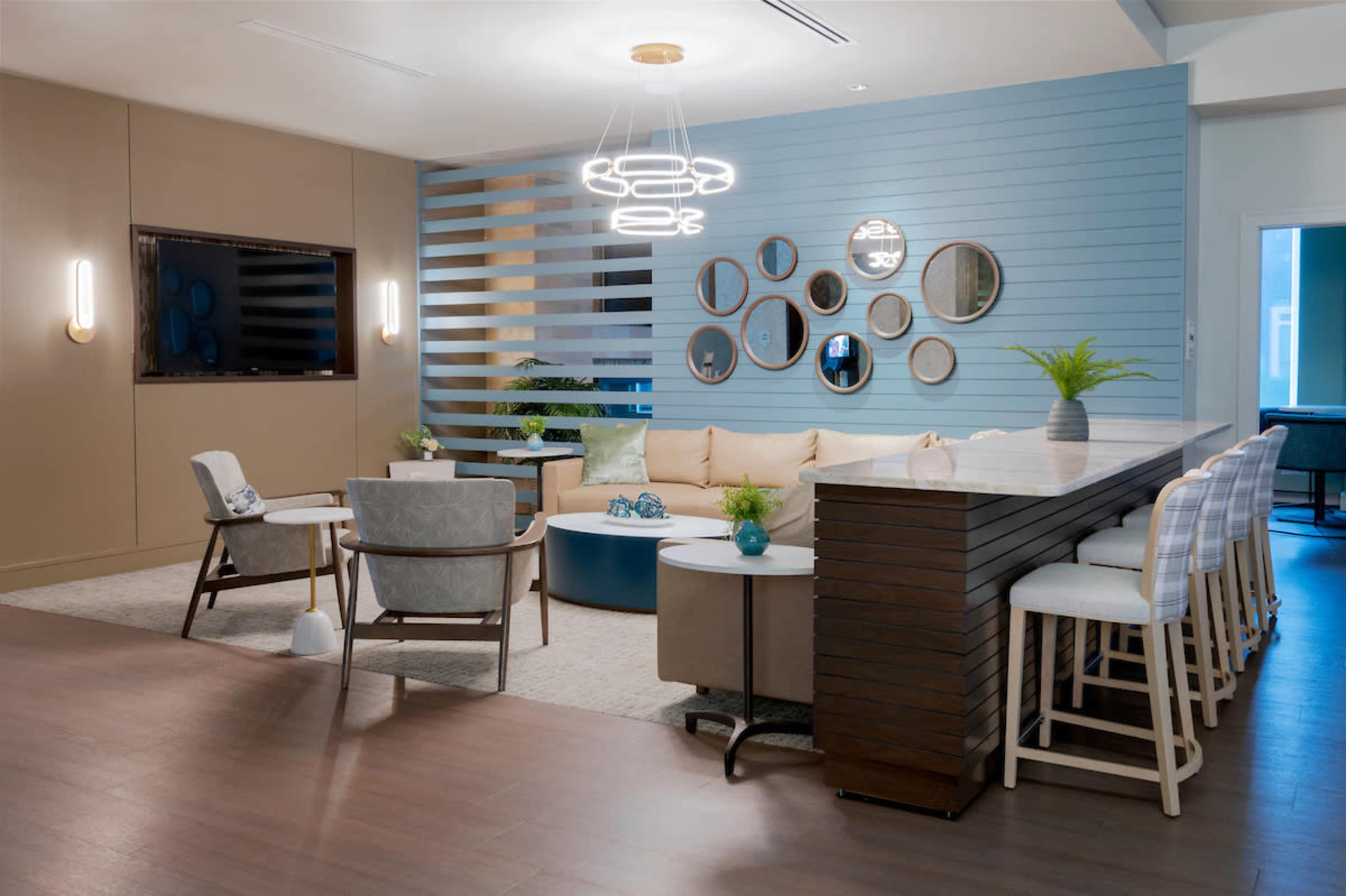 A modern lounge area featuring a sectional sofa, a bar with stools, and a decorative wall with mirrors and plants.