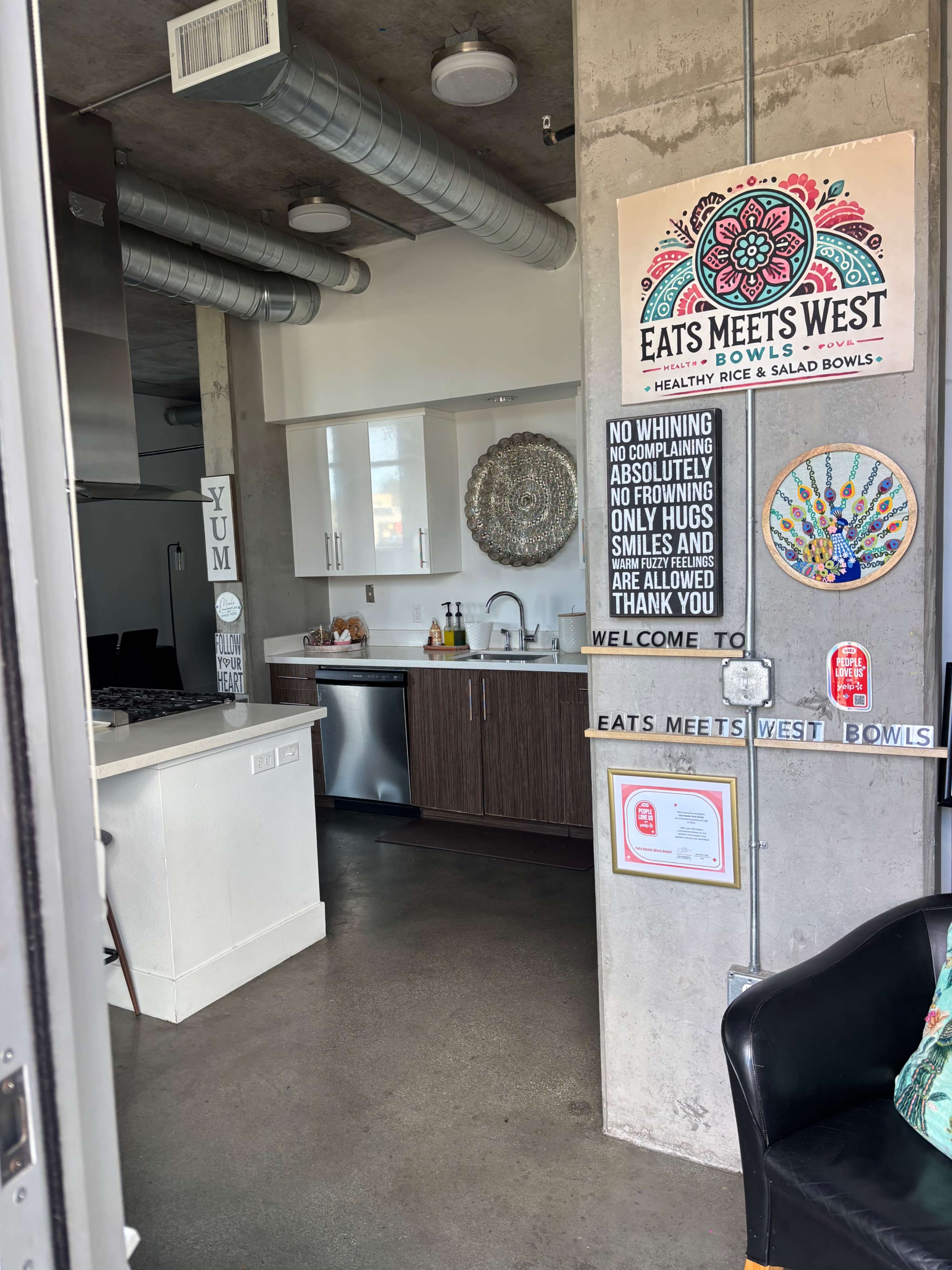 The image shows a modern kitchen area in an apartment, featuring stainless steel appliances and a decorative wall with various signs and artwork.