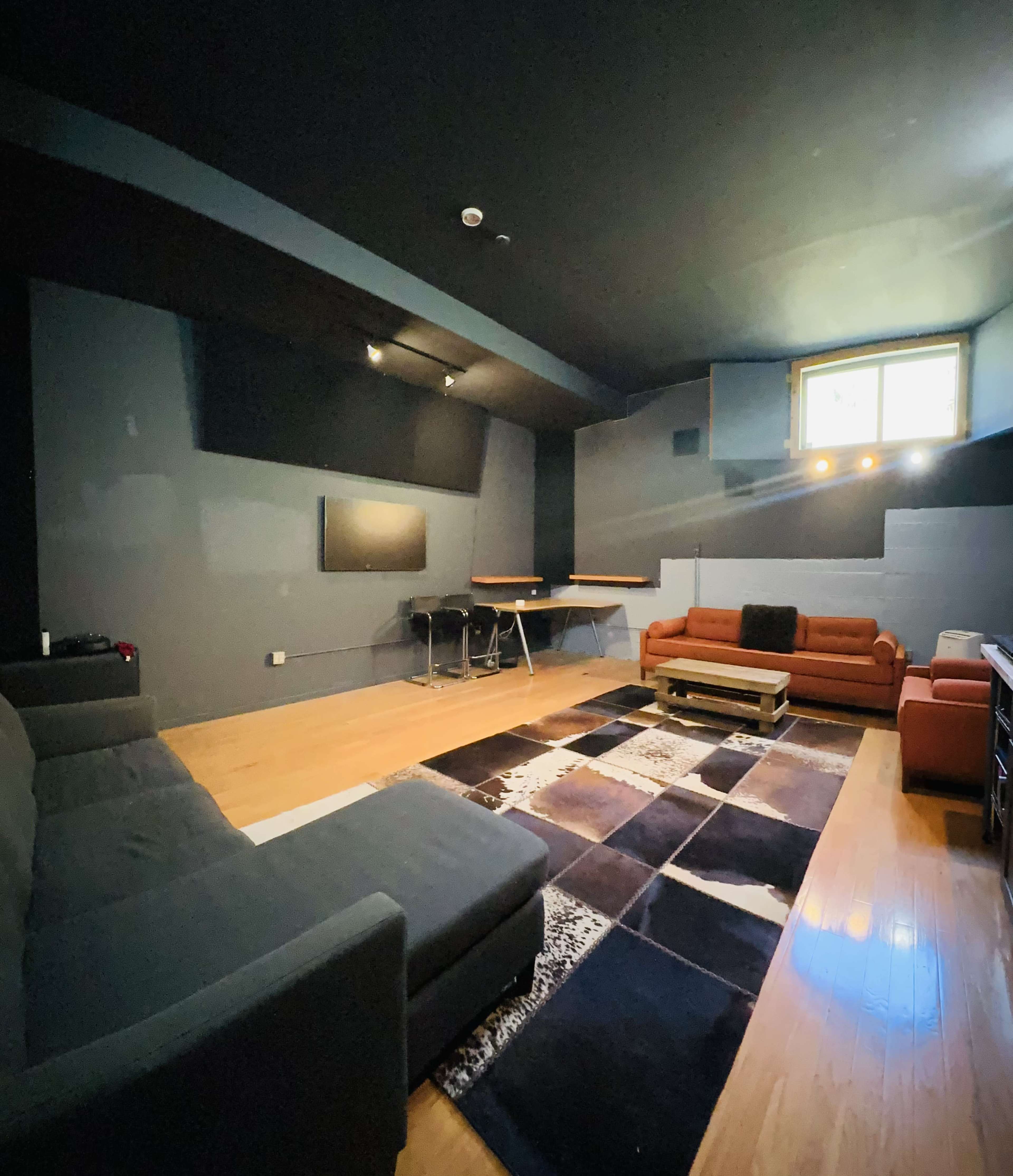 The room features two sofas, a coffee table, and a large area rug, with a wall-mounted television and a table set against the background of dark walls and a ceiling.