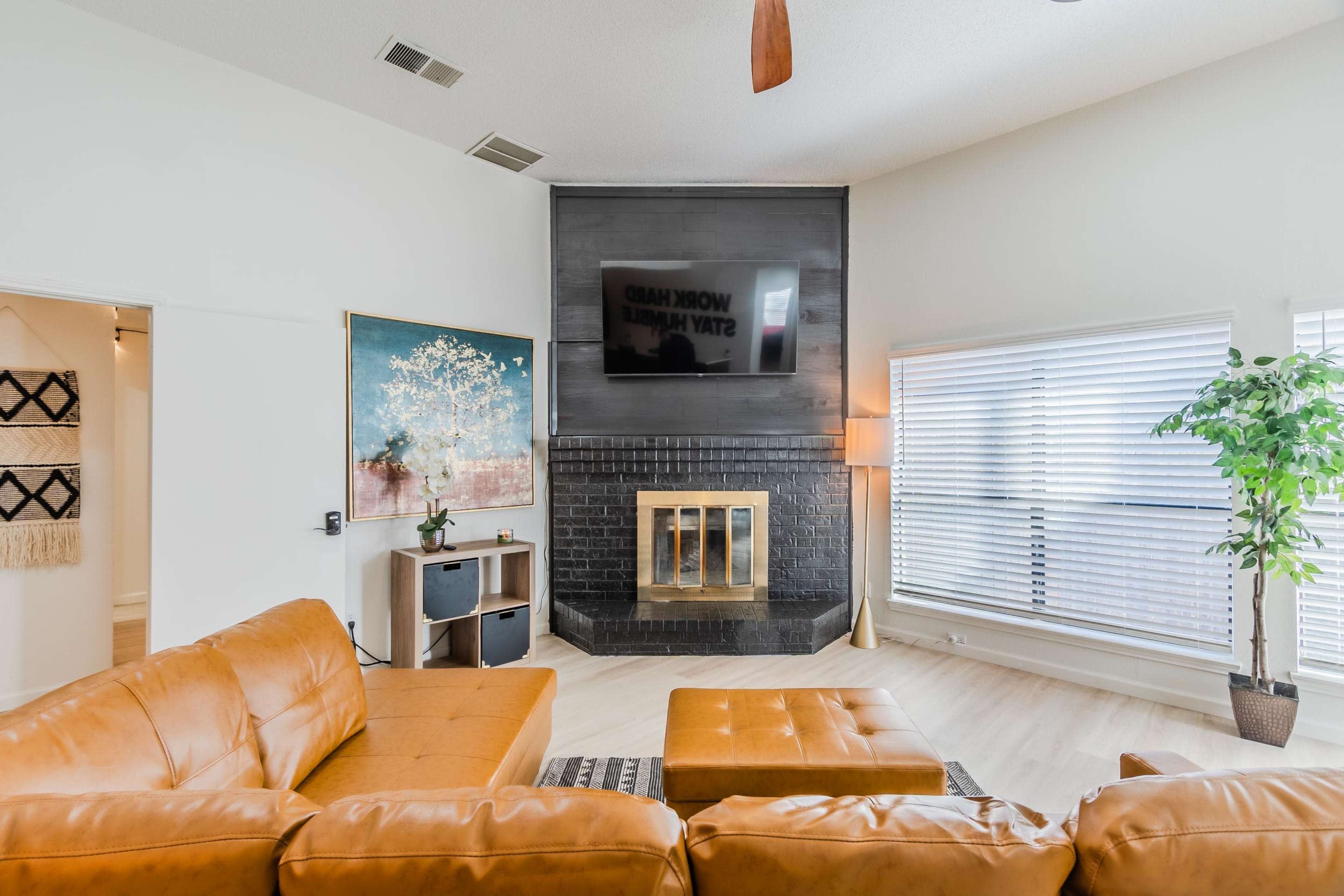 A modern living room featuring a large brown leather sectional sofa, a black fireplace with a mounted television, and a decorative painting on the wall.