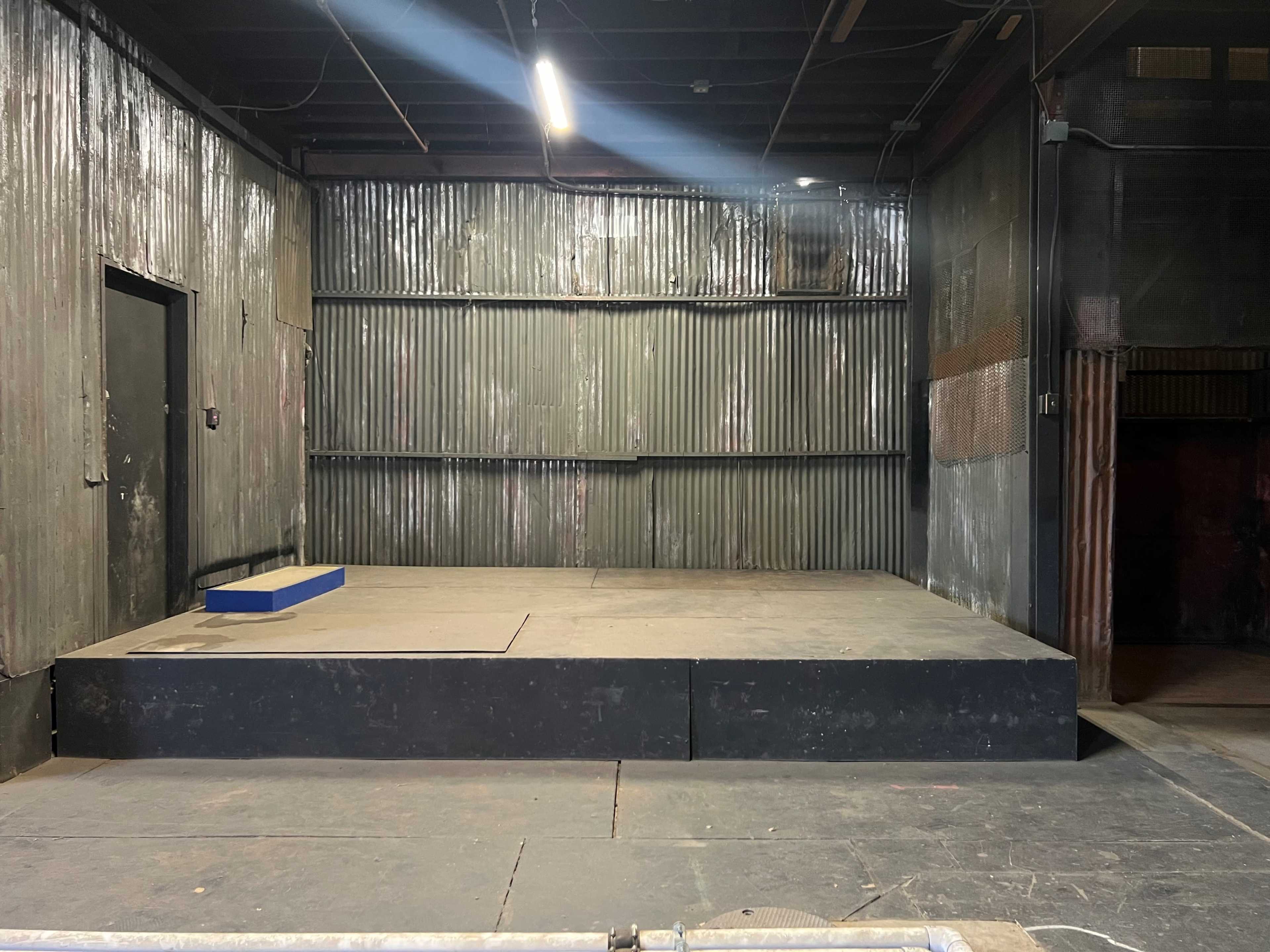 A dimly lit stage with a raised platform and a metal wall behind it.