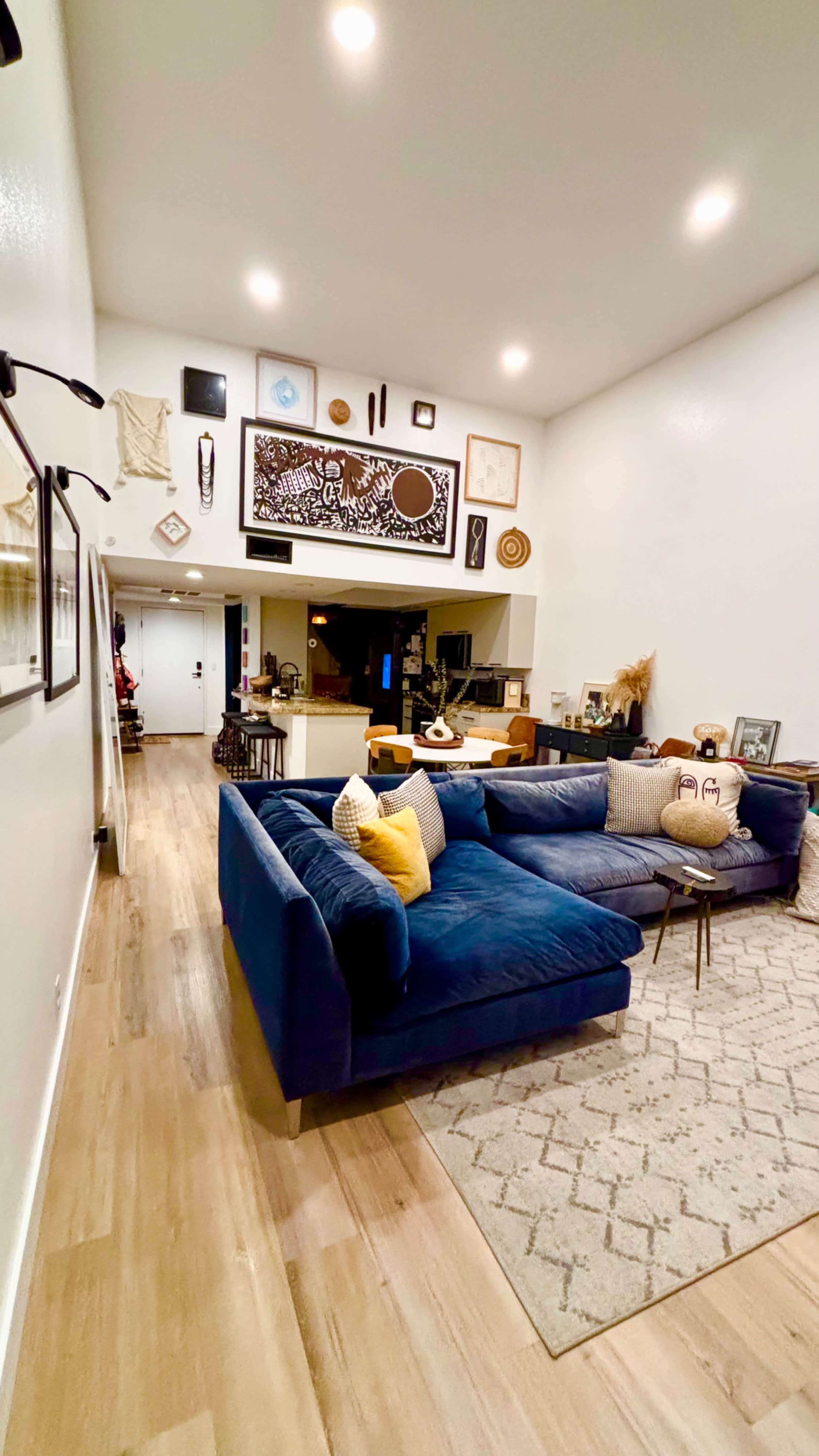 A spacious living room features a large blue sectional sofa, a decorative area rug, and various artworks displayed on the walls.